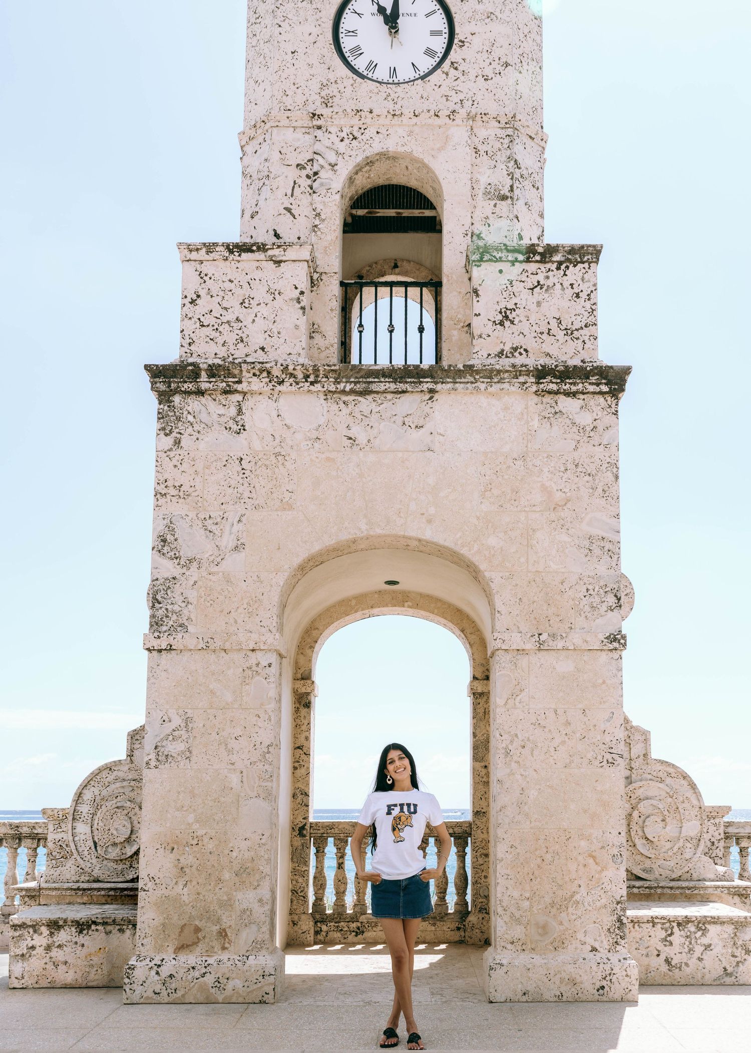 Woman standing under stone arch of historic clock tower against blue sky on Worth Avenue Palm beach.