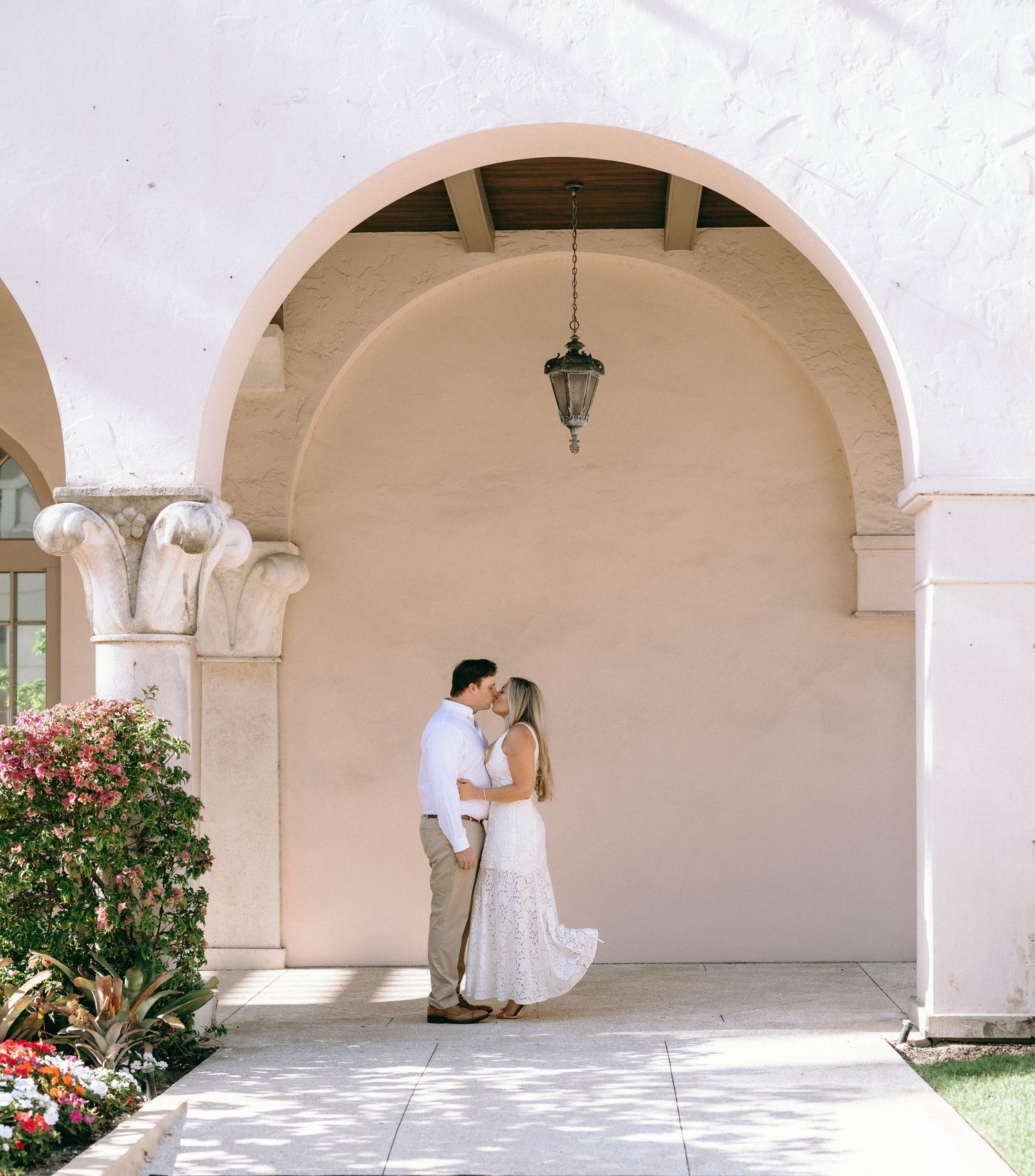 Couple sharing a romantic kiss under a Spanish-style archway with pink walls and hanging lantern.