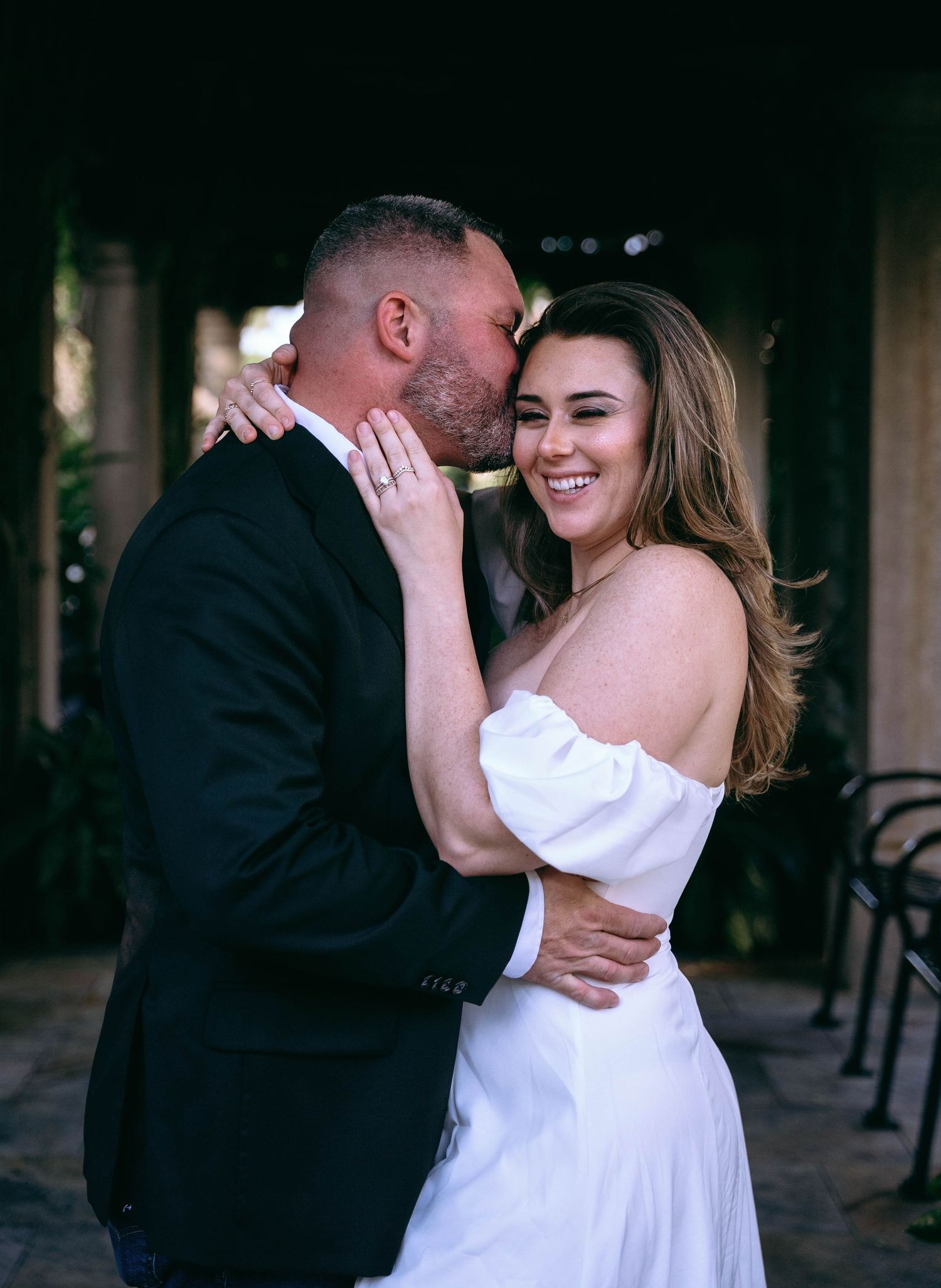 A romantic couple shares an intimate moment in formal attire against a dark background.