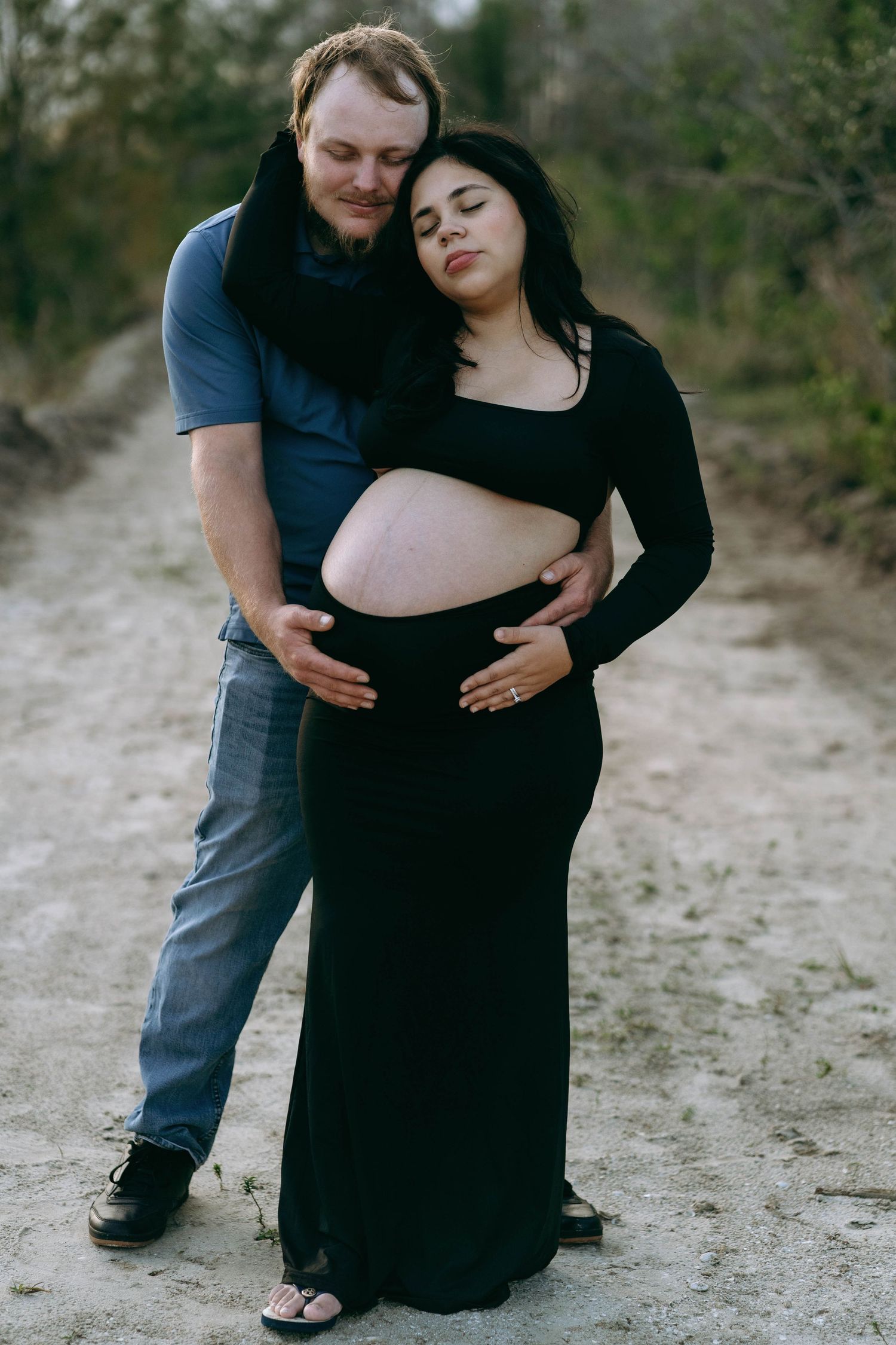 A couple embraces while sitting on sandy ground during an intimate outdoor photoshoot.