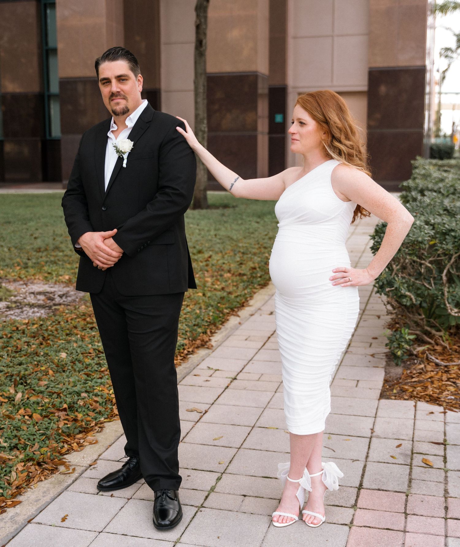 Wedding couple poses playfully on stone pathway with classic architecture in background.
