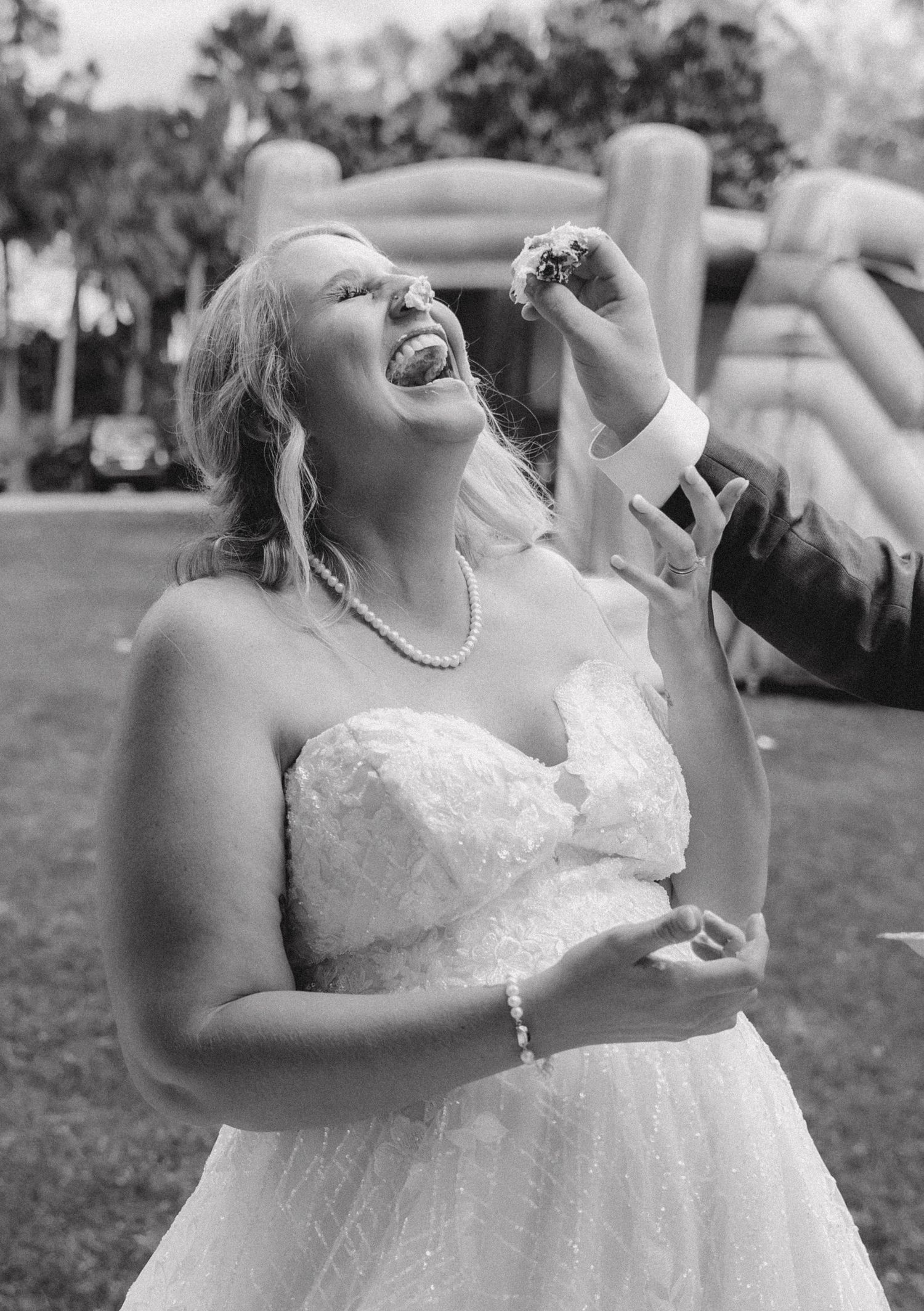 Joyful moments captured as bride enjoys wedding cake at outdoor reception.
