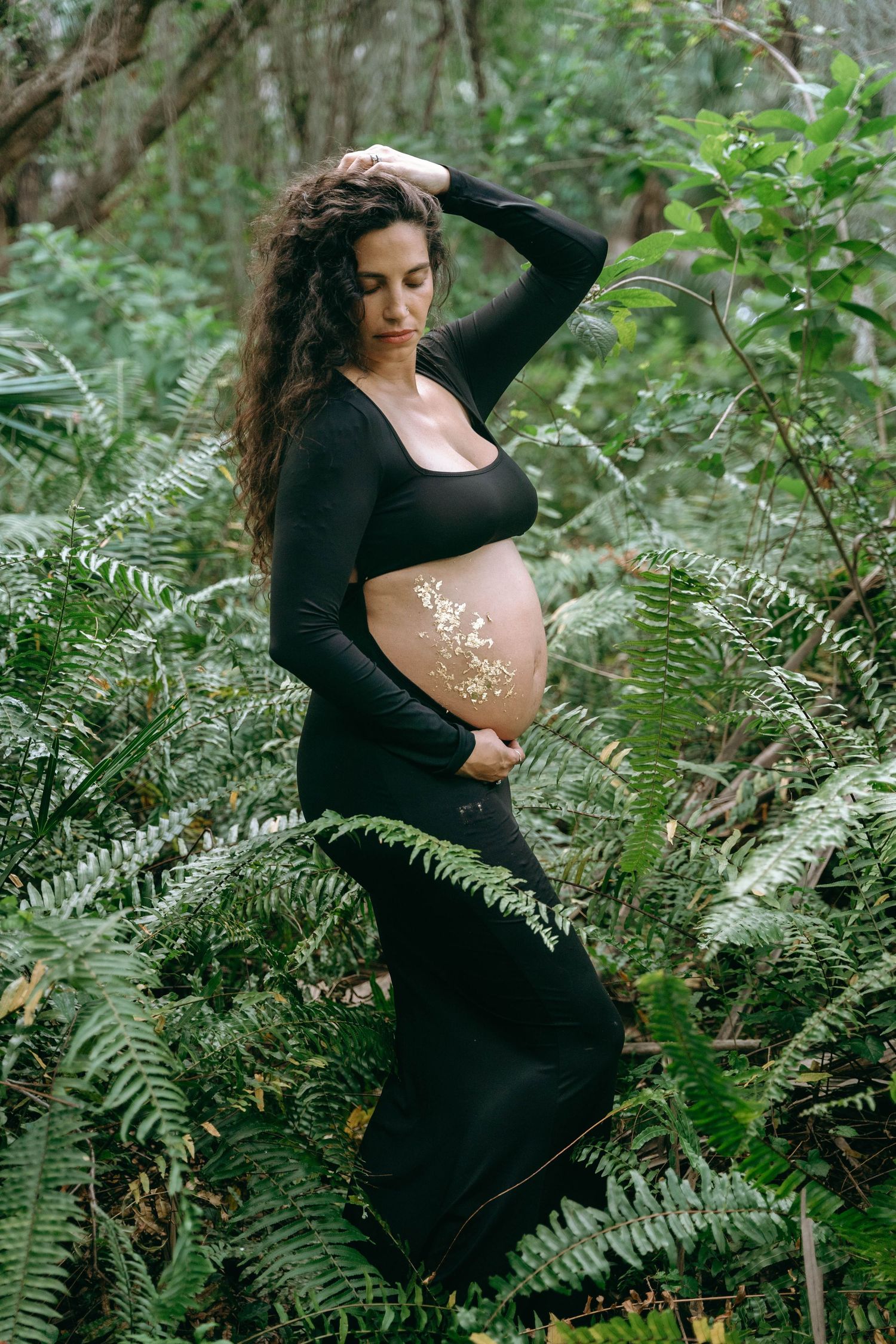 Artistic maternity portraits in black dress surrounded by wild ferns and forest foliage.