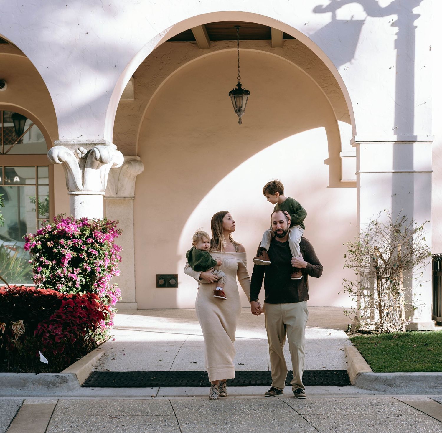 Family playfully interacting under Mediterranean style arches with pink flowers in the background.