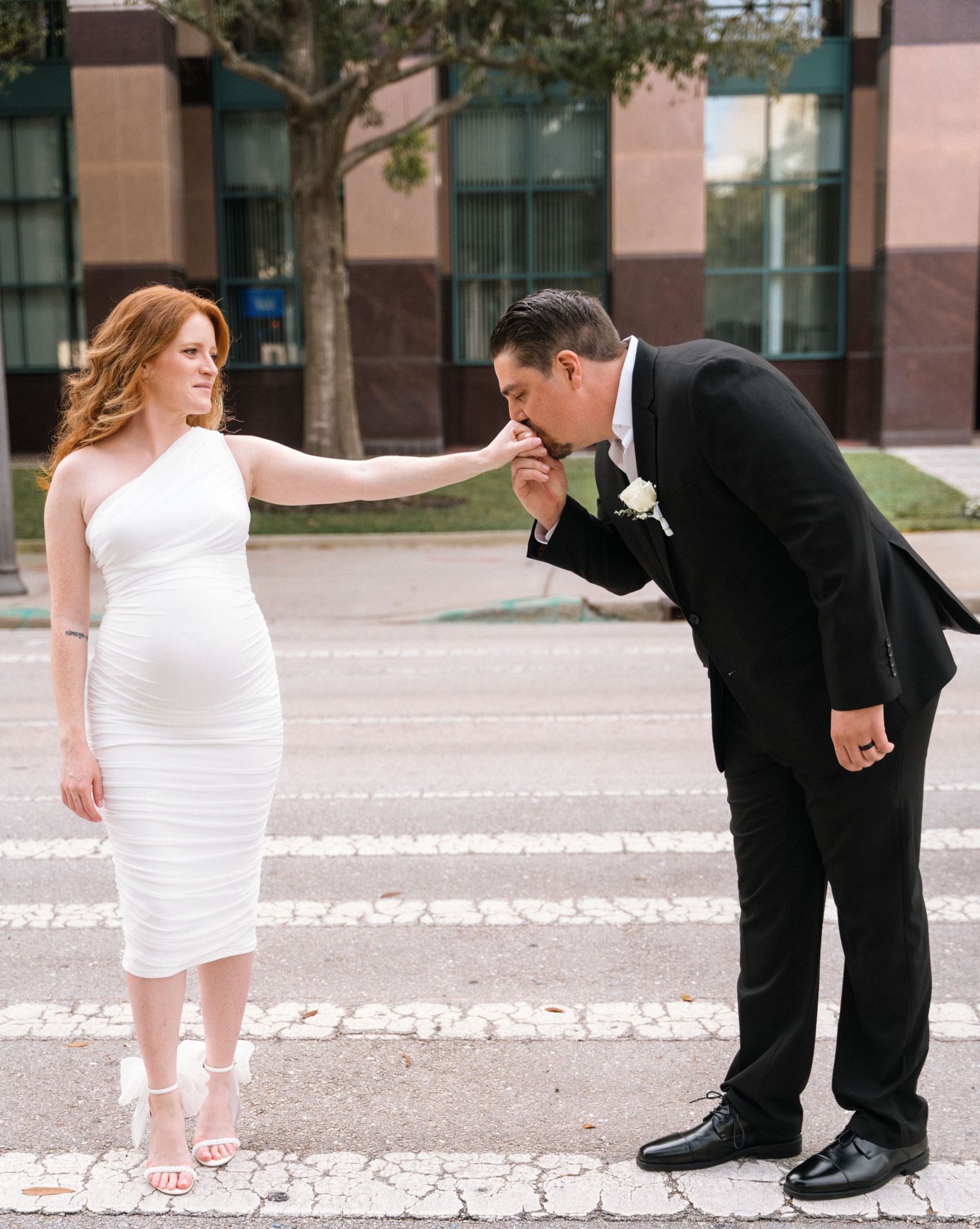 A romantic wedding moment captured as groom kisses bride's hand on a striped pedestrian crossing.