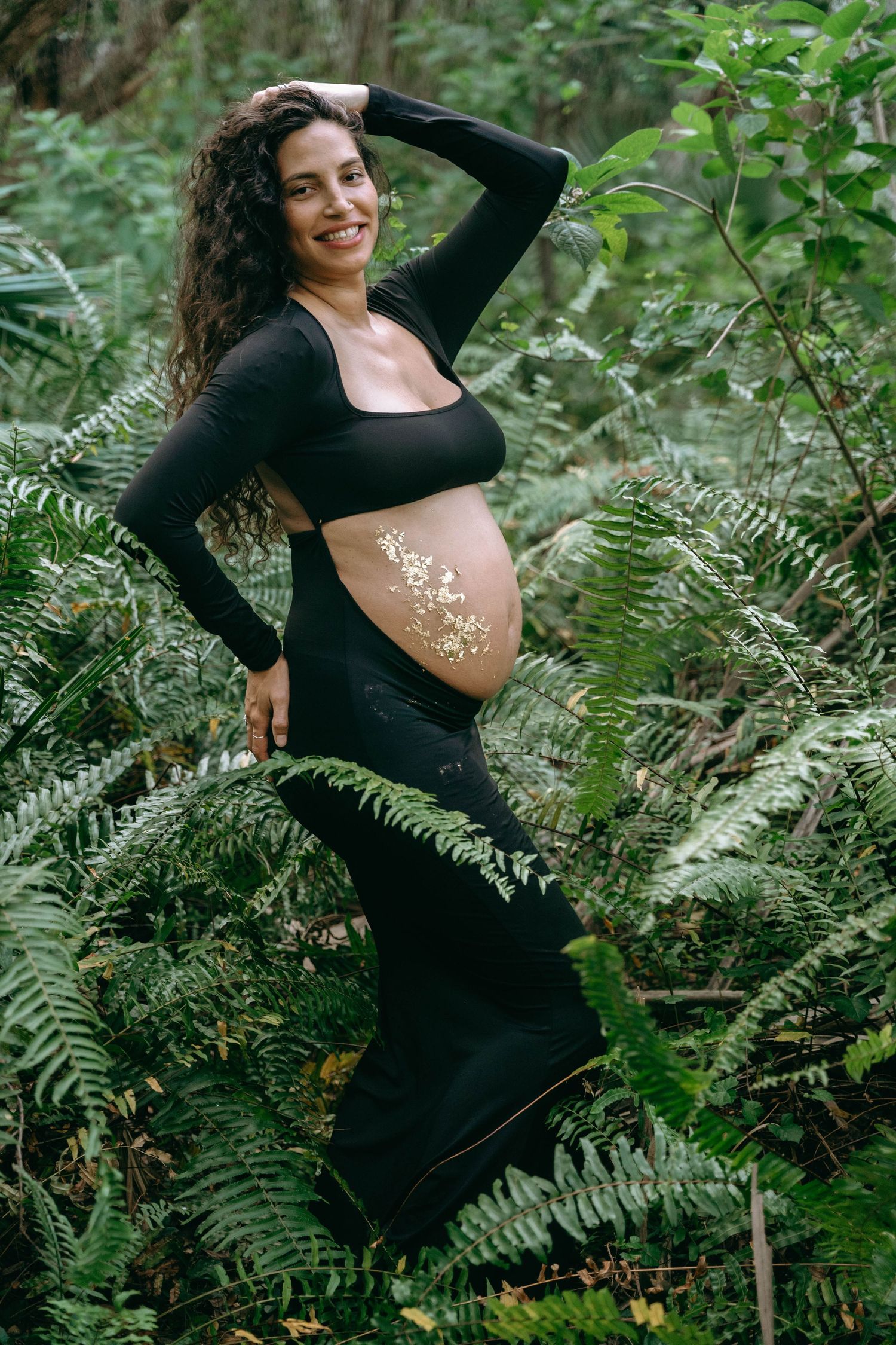 Maternity photoshoot in a lush forest setting with ferns and greenery.
