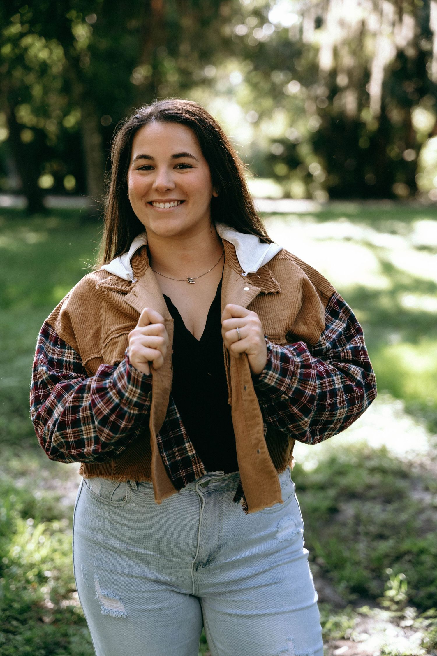 Person wearing plaid jacket and jeans poses playfully in outdoor setting.