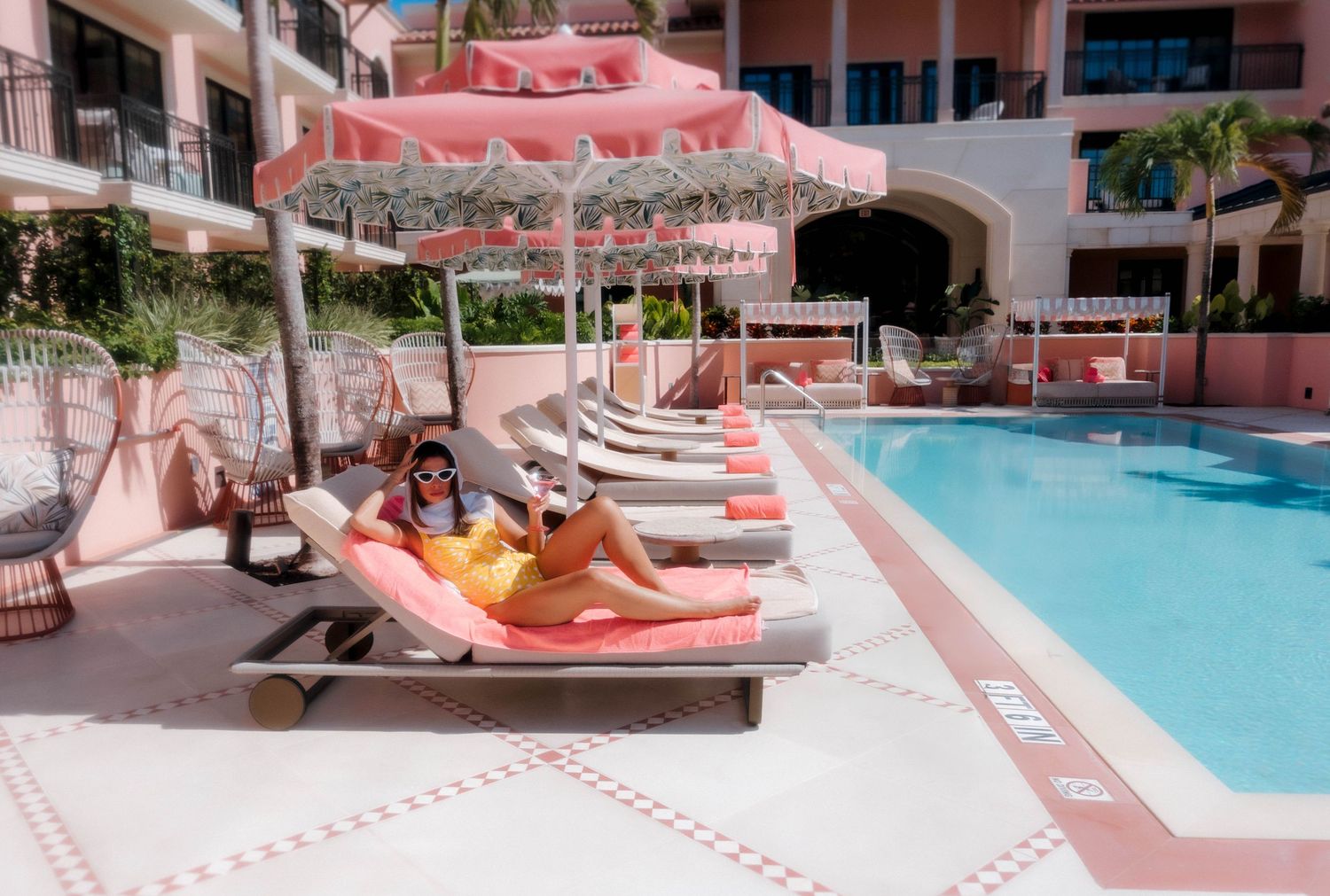 Pink-tinted resort poolside scene with lounge chairs and umbrellas.