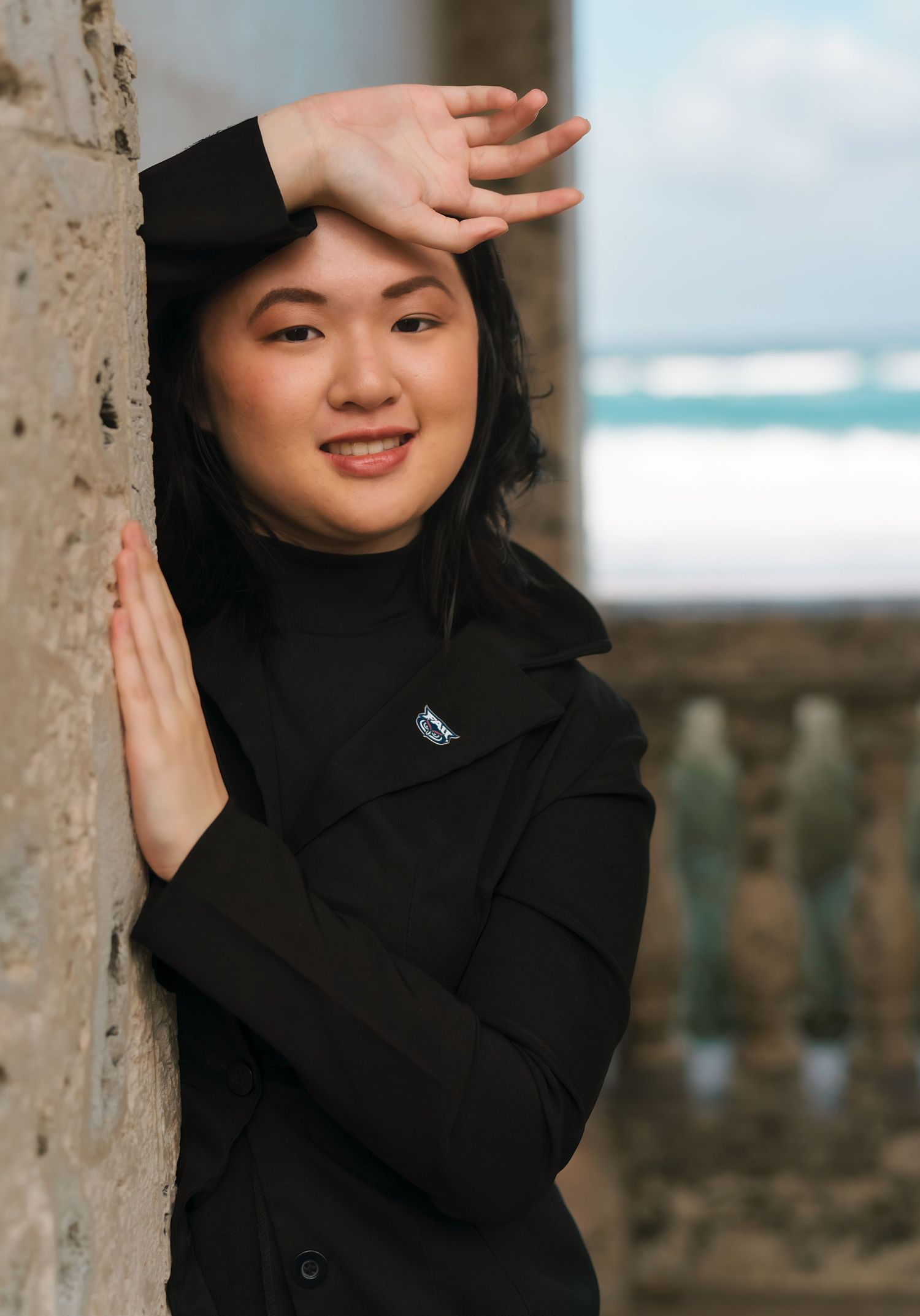 A stylish black coat photographed against stone columns with ocean views.