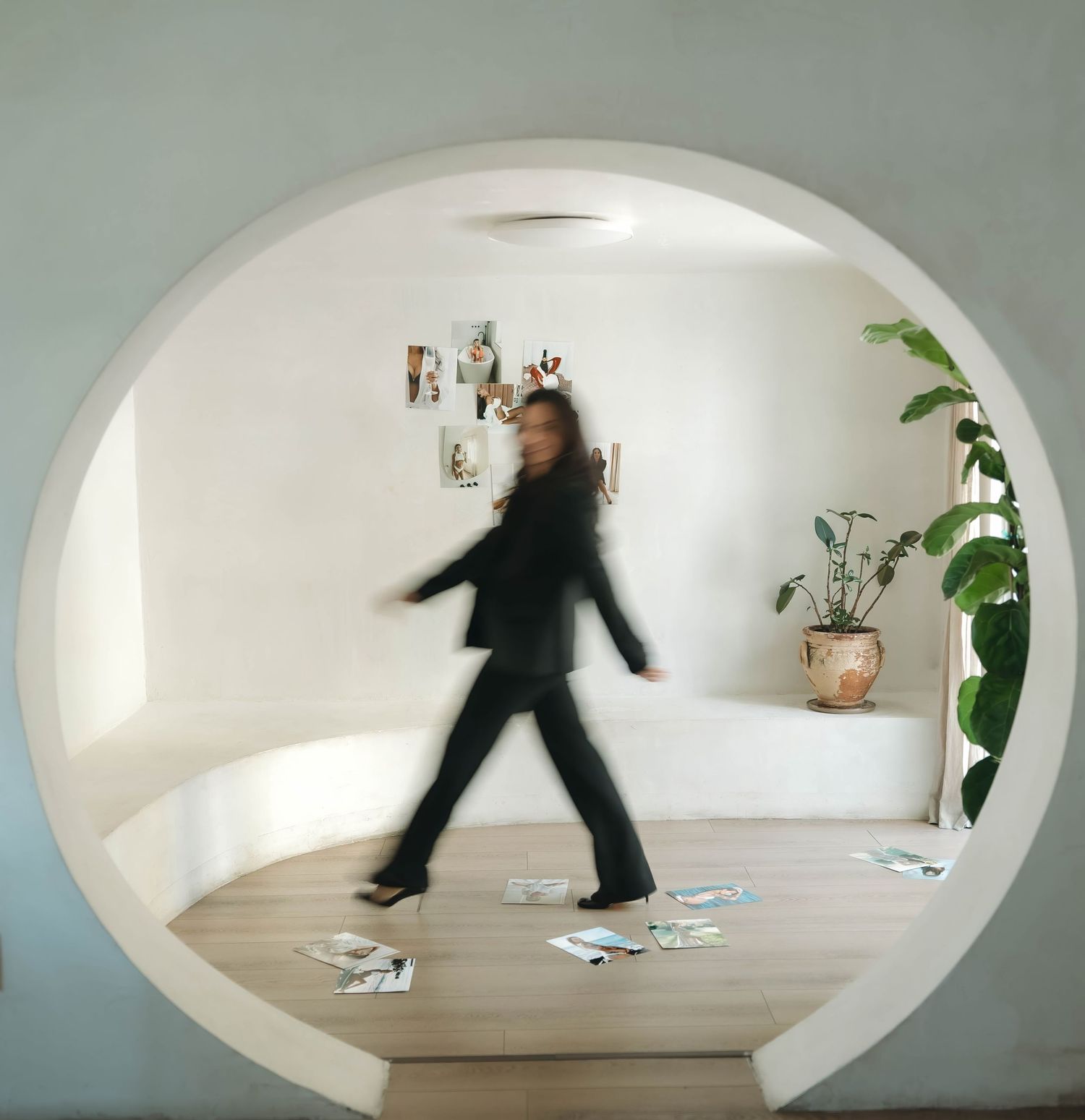 A blurred figure in black clothing walks through a circular doorway with photos on wall.