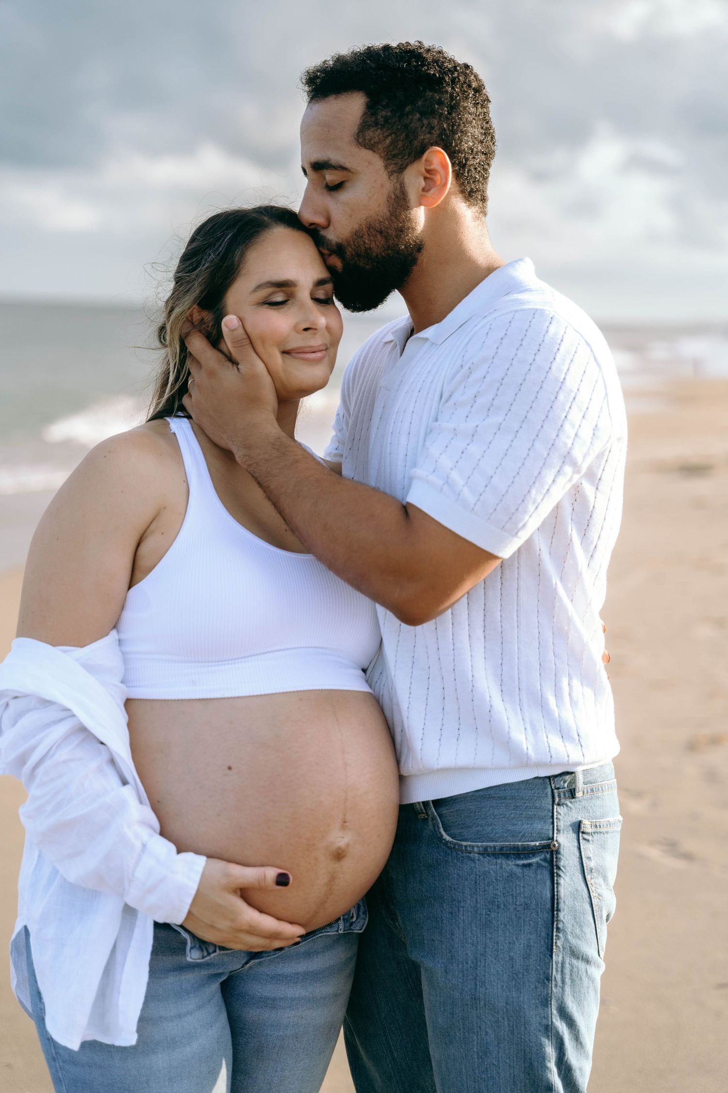 A romantic beach photoshoot series showing tender moments between a couple in white and denim outfits.