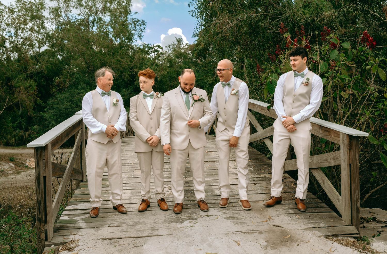 Five people in white attire sit casually on a wooden fence during an outdoor photoshoot.