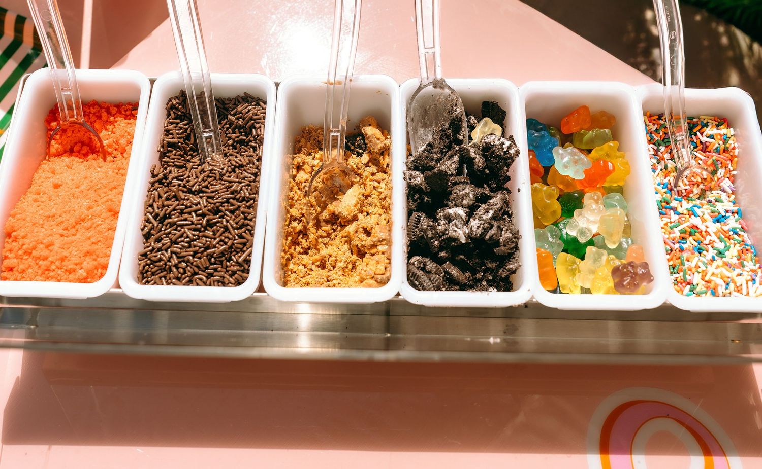 Colorful ice cream toppings bar with sprinkles, chocolate chips, cookie crumbles, Oreos, gummy candies, and rainbow sprinkles.
