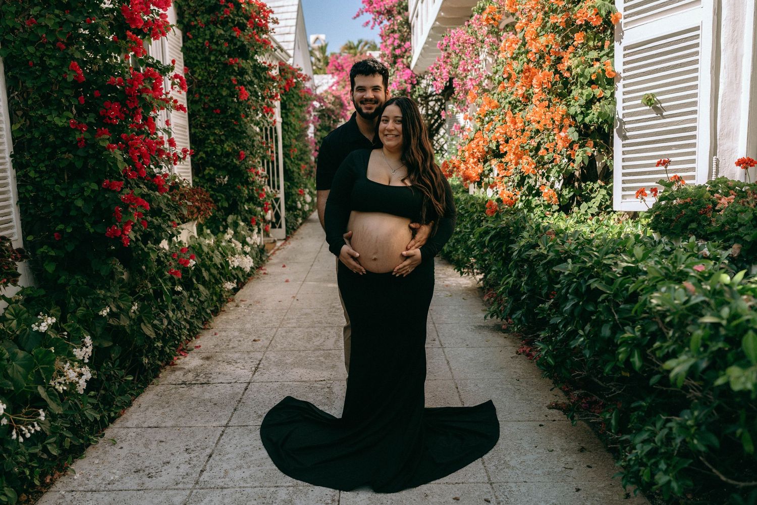 Couple in black outfits posing for maternity photo surrounded by colorful bougainvillea flowers. Worth Avenue, Palm Beach, FL