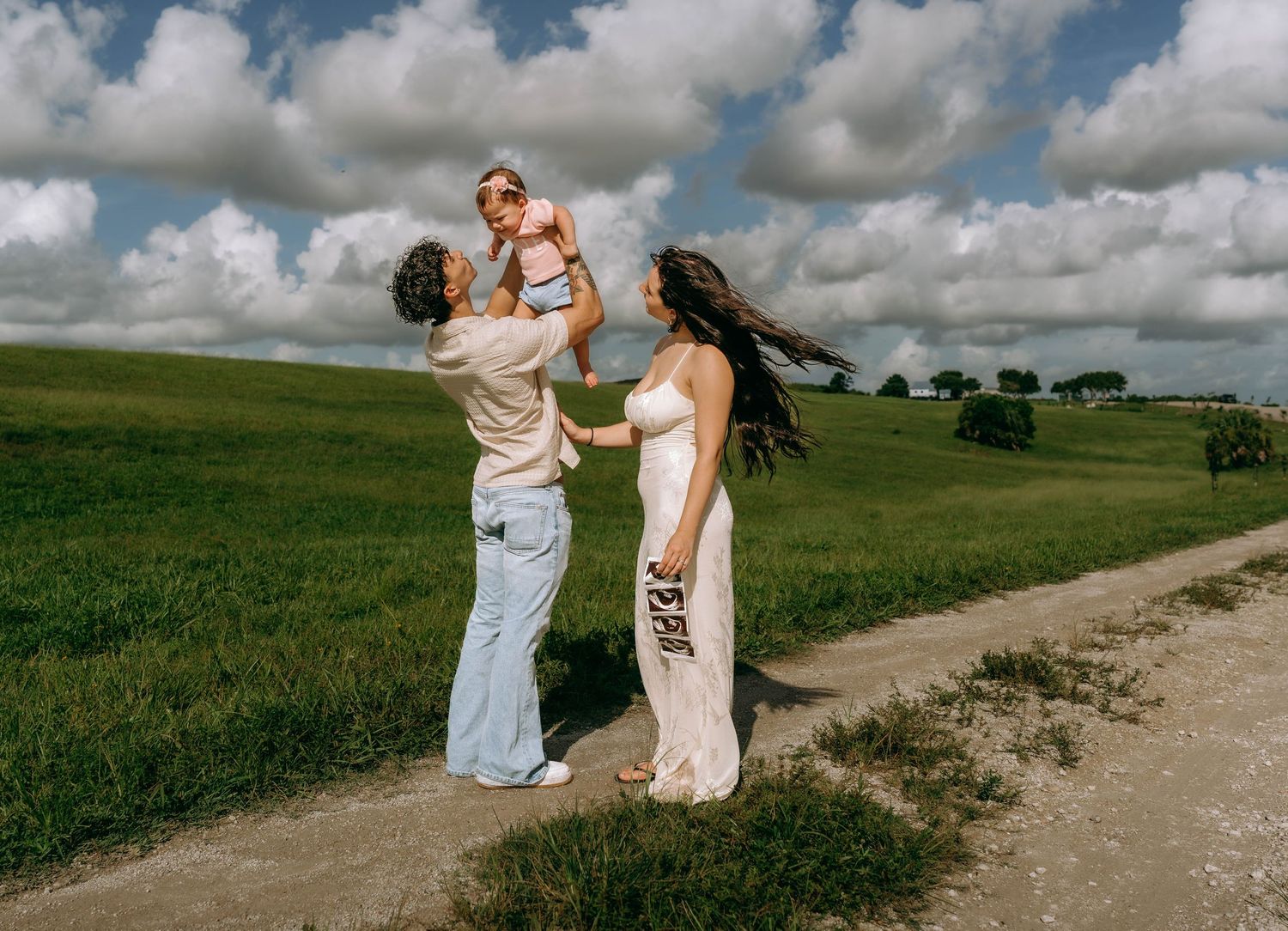 Family with baby enjoying a sunny day on a green countryside path under dramatic cloudy skies.