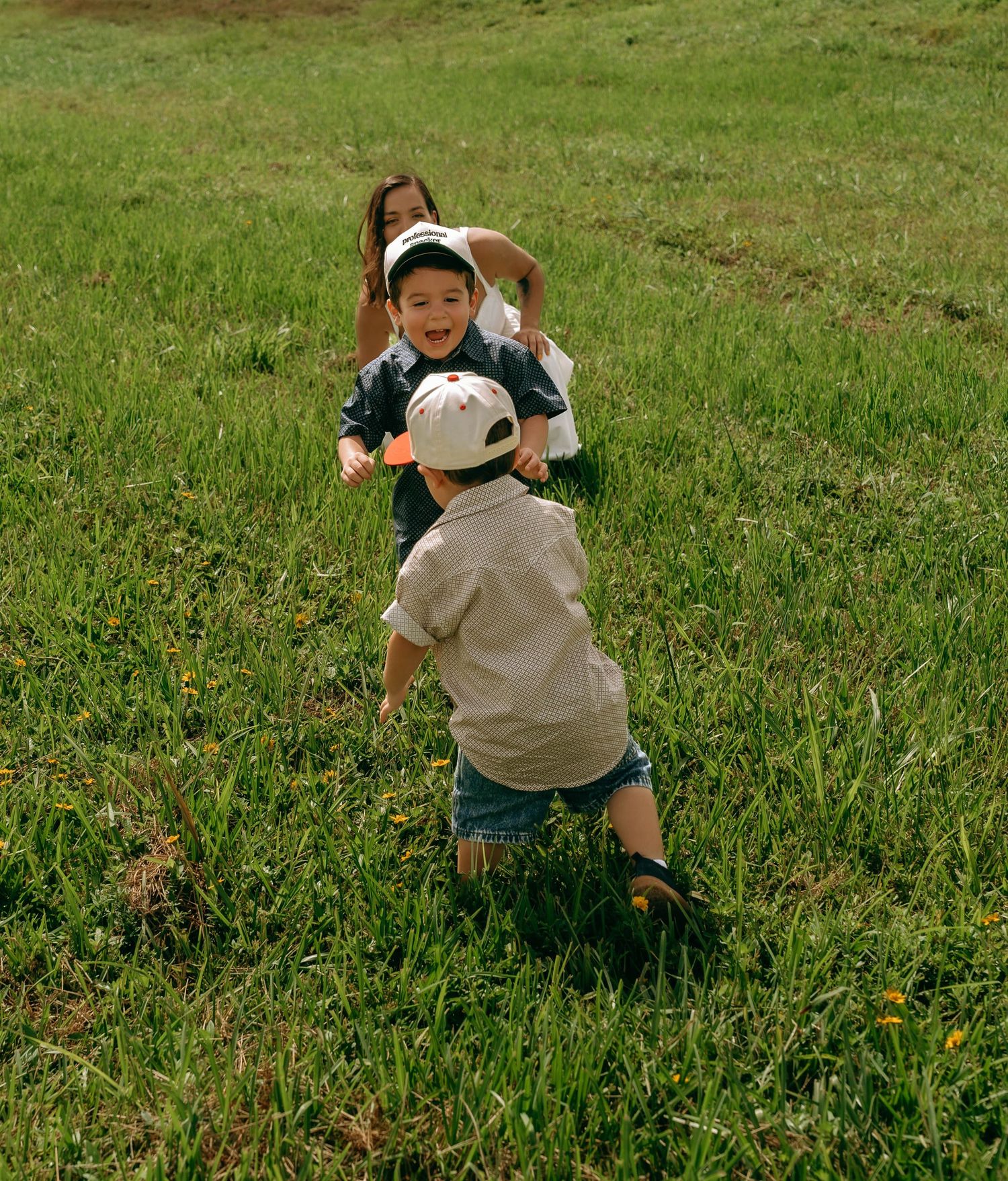 Three children playing joyfully in a lush green grass field on a sunny day.