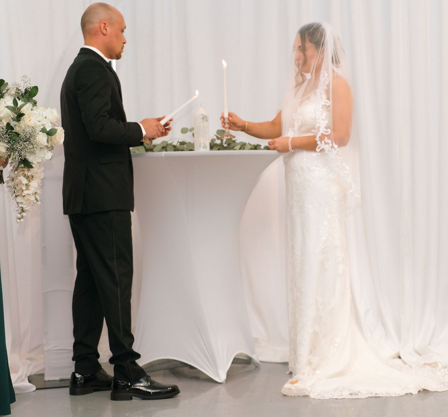 Wedding ceremony participants standing at altar with white draping and candles.
