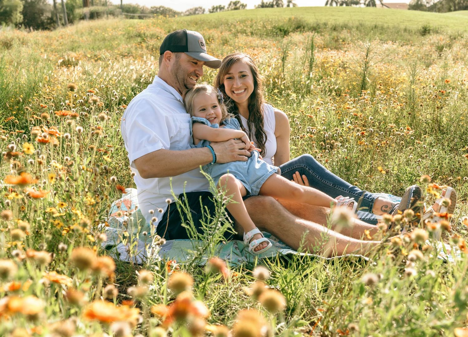 Happy family sitting in a wildflower meadow, parents smiling with young child on sunny day.