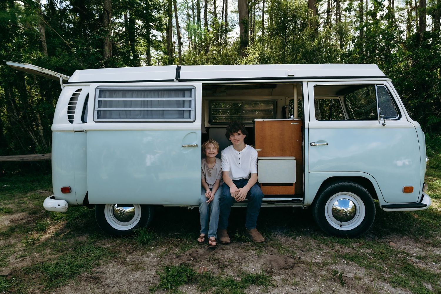 Classic white Volkswagen van parked in a wooded area with doors open.