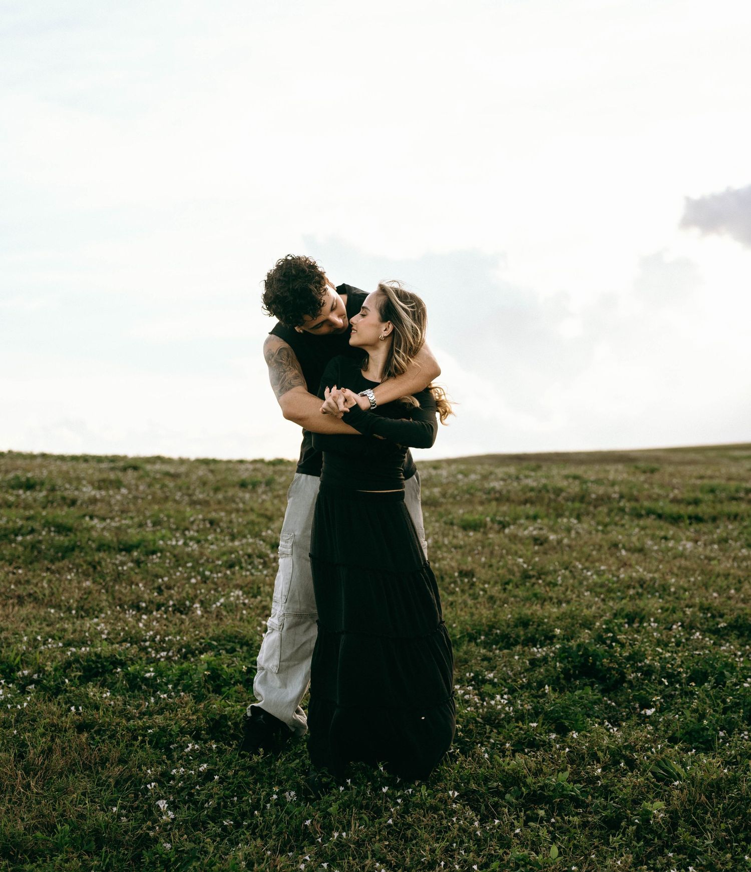 A couple shares an intimate moment while dancing in a meadow.