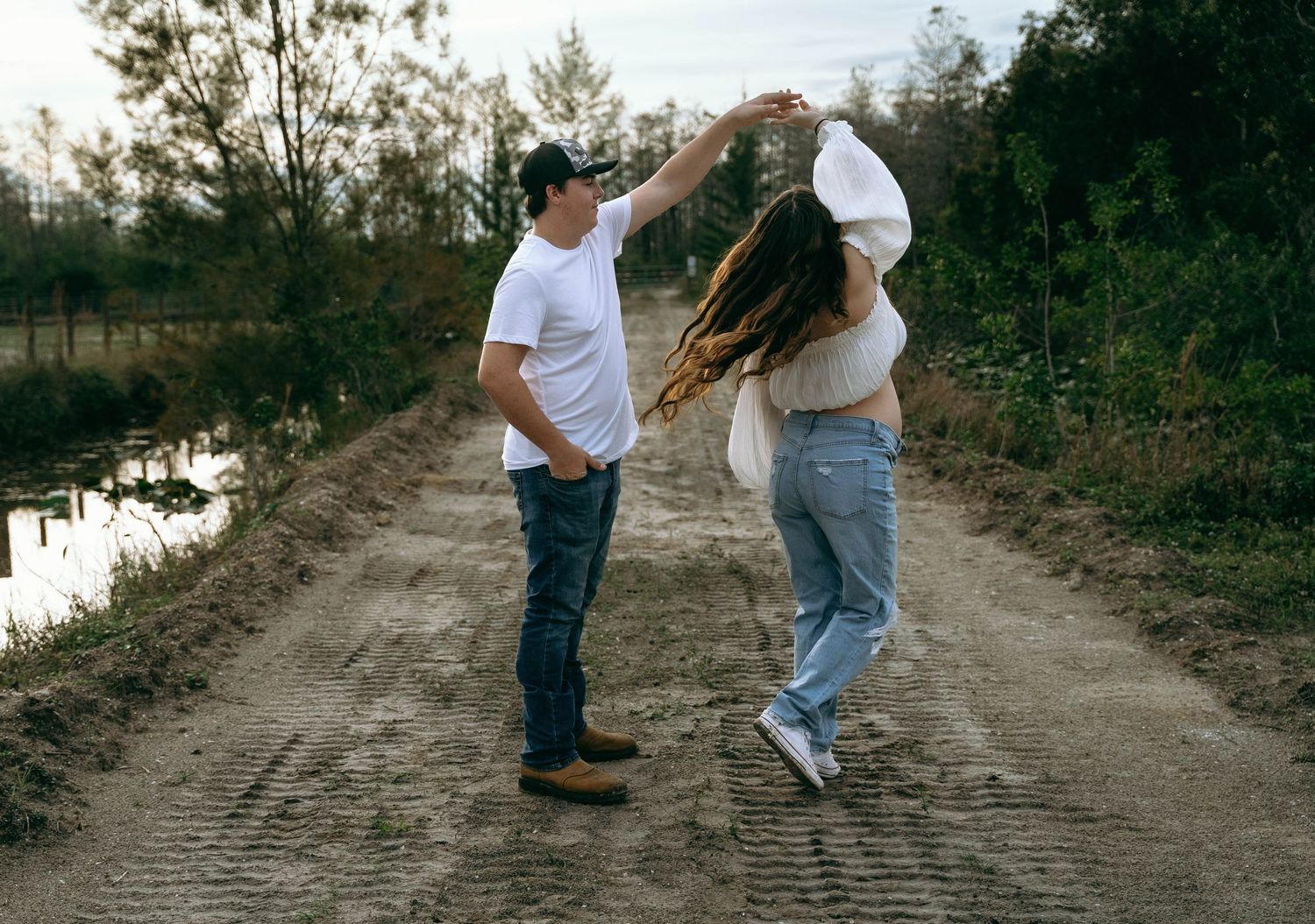 A couple walks together on a dirt path surrounded by greenery in a romantic outdoor setting.
