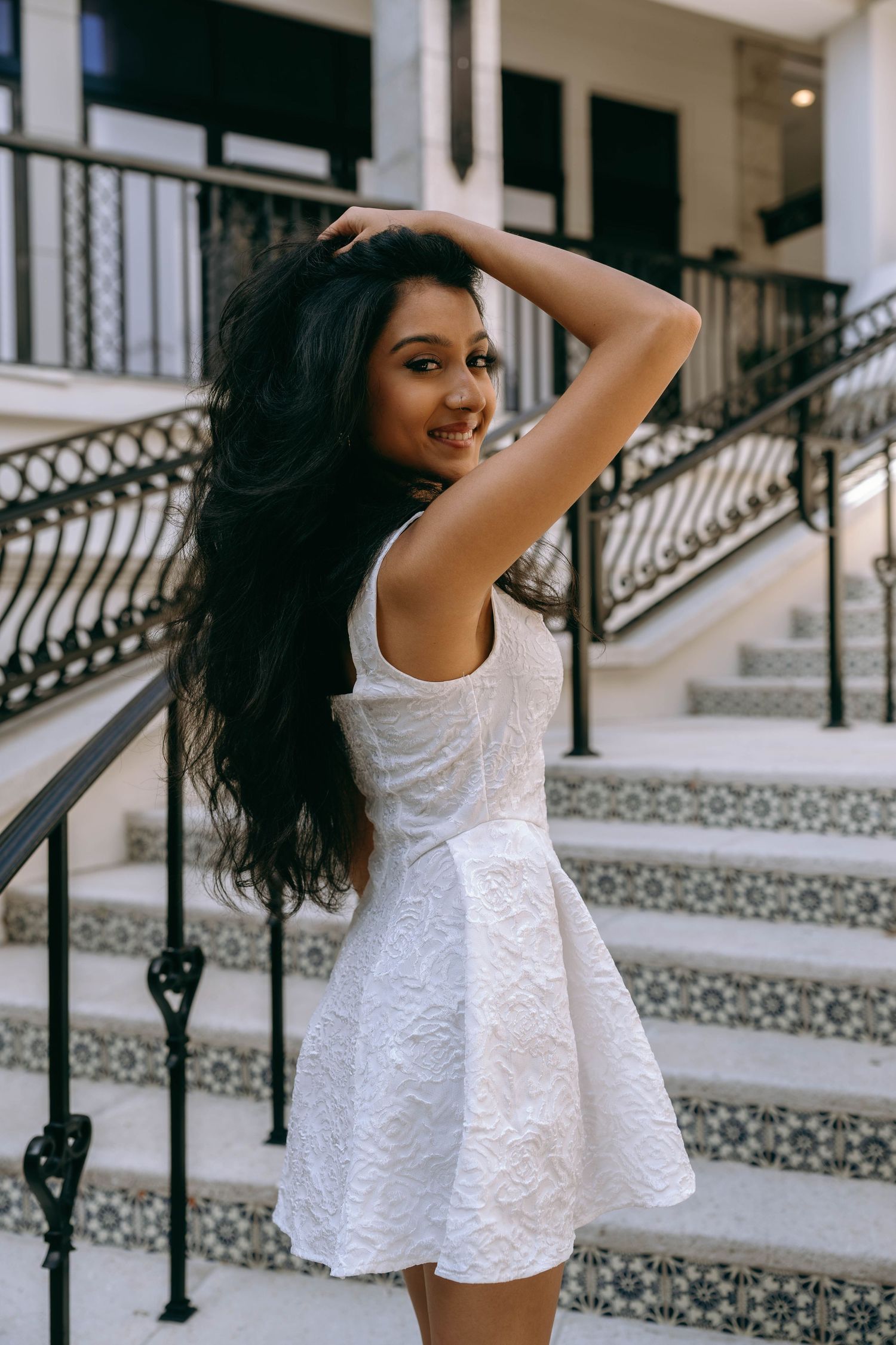 Young woman in white dress posing on decorative tiled staircase with iron railings on Worth Avenue Palm beach.