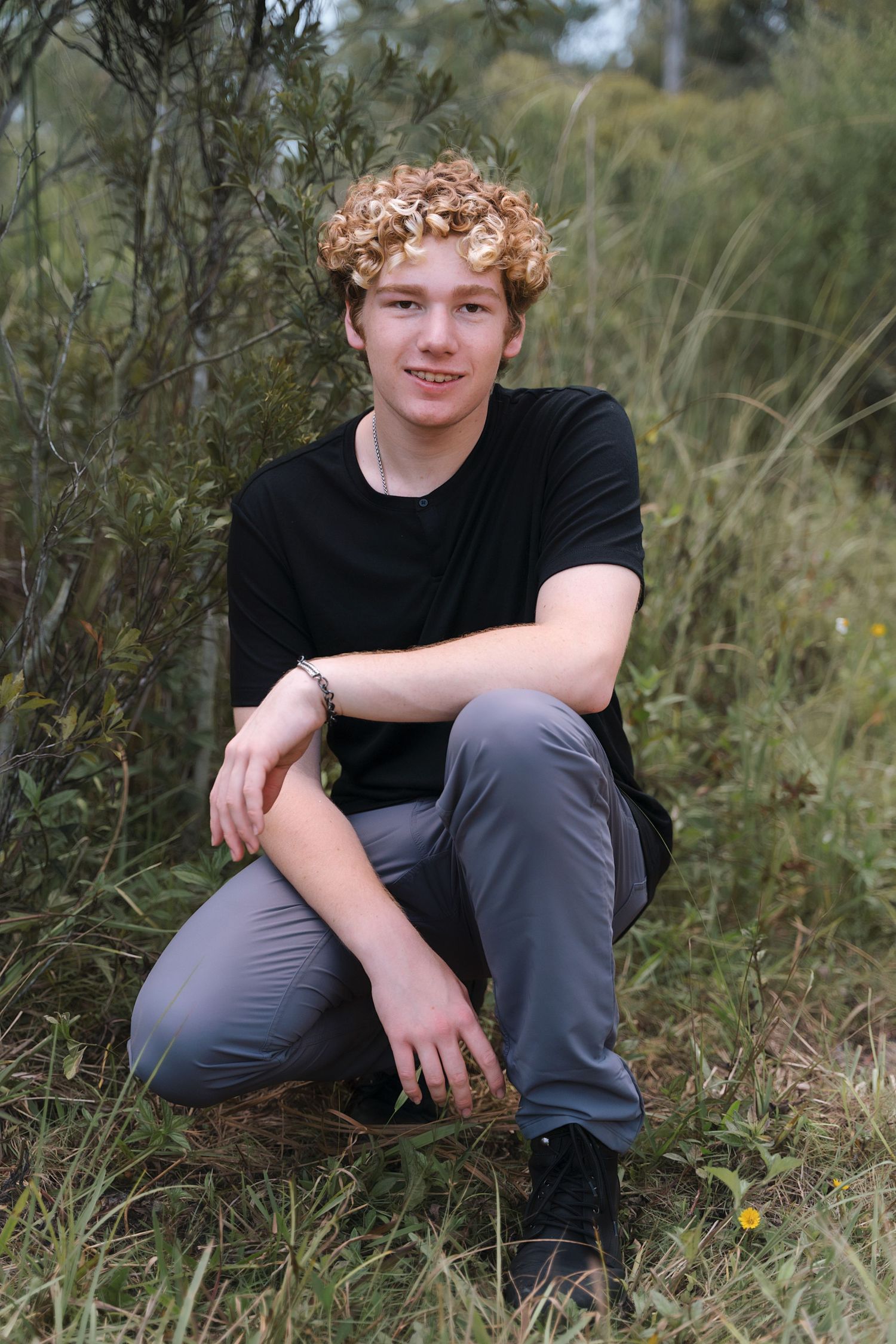 Casual outdoor portrait session in black shirt and gray pants among tall grass.