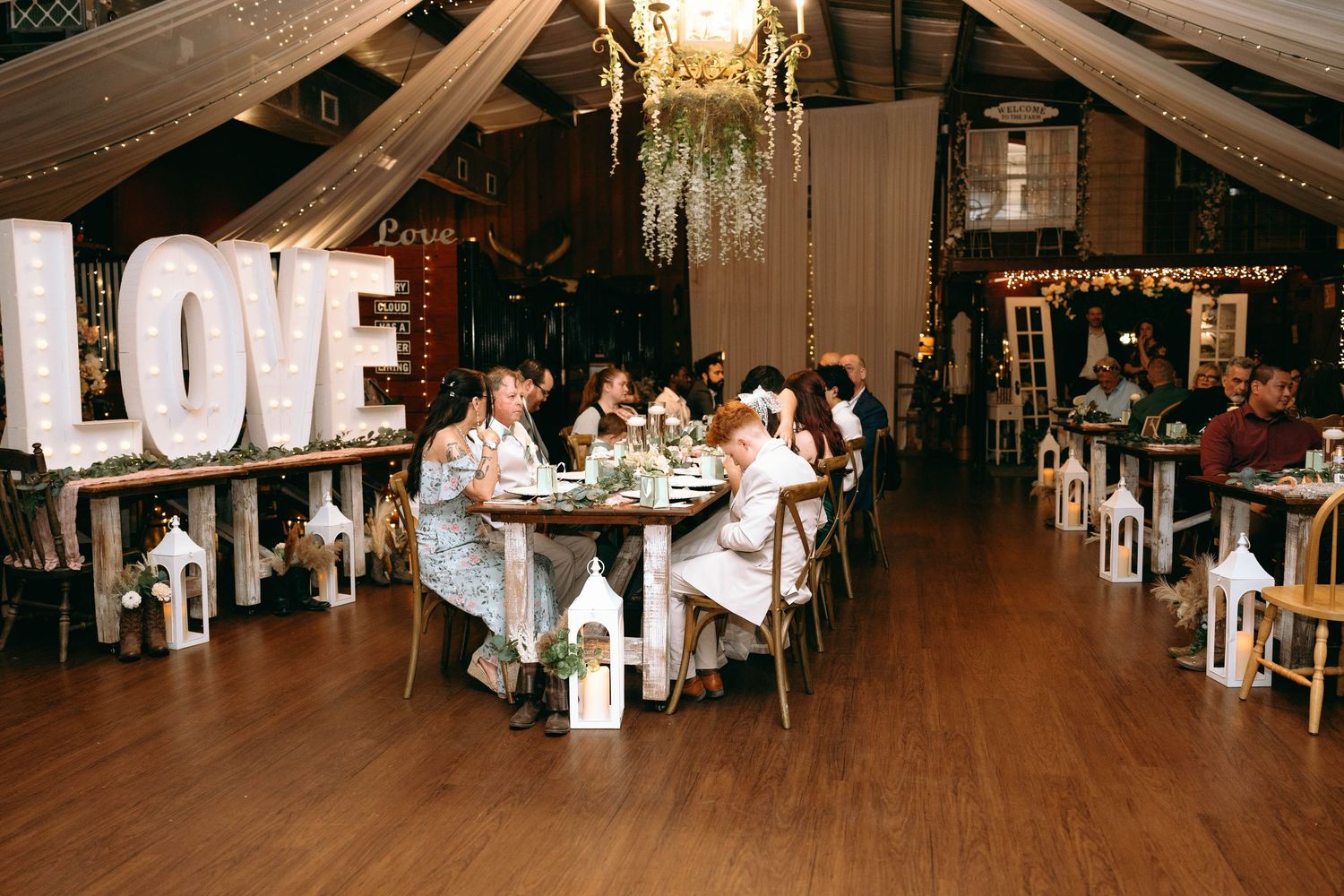 Wedding reception venue with large LOVE marquee letters and guests dining at round tables on wooden floors.