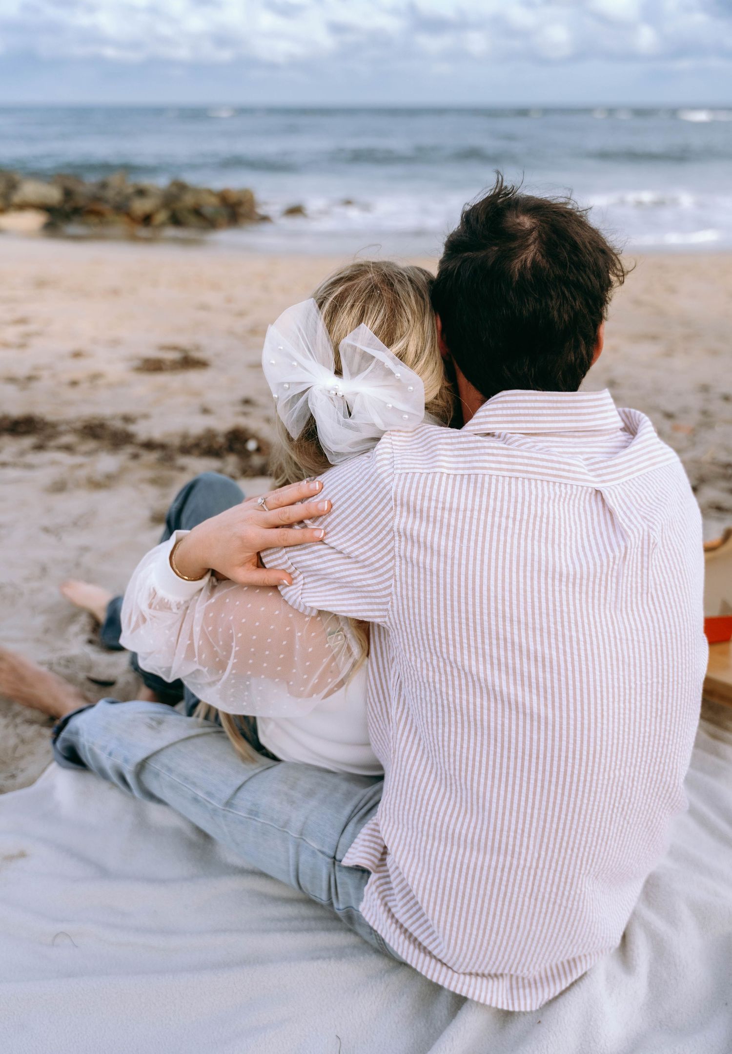 Couple relaxing together on a sandy beach with ocean waves in the background.