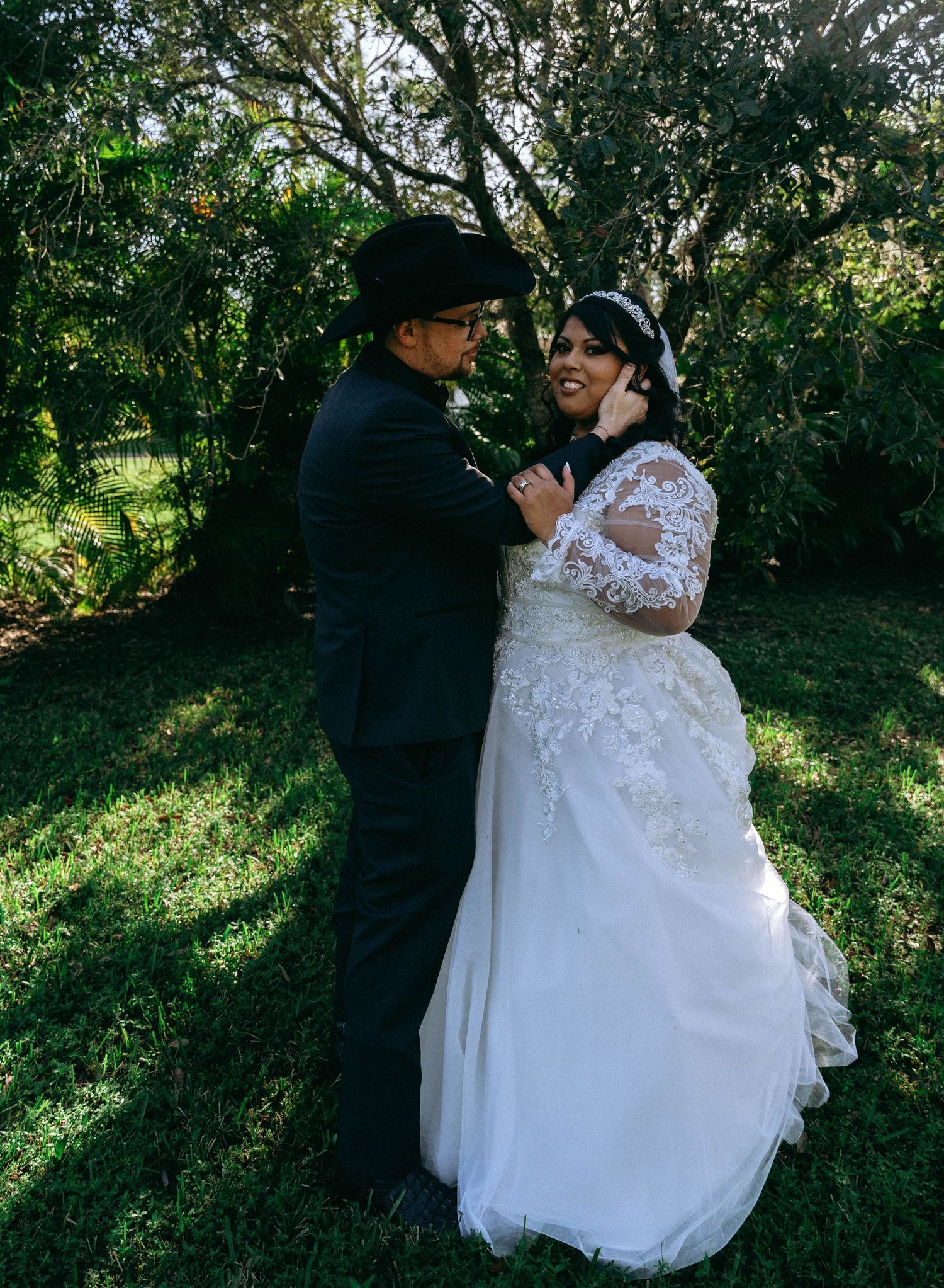 Newlyweds share intimate moment in garden setting wearing formal attire.
