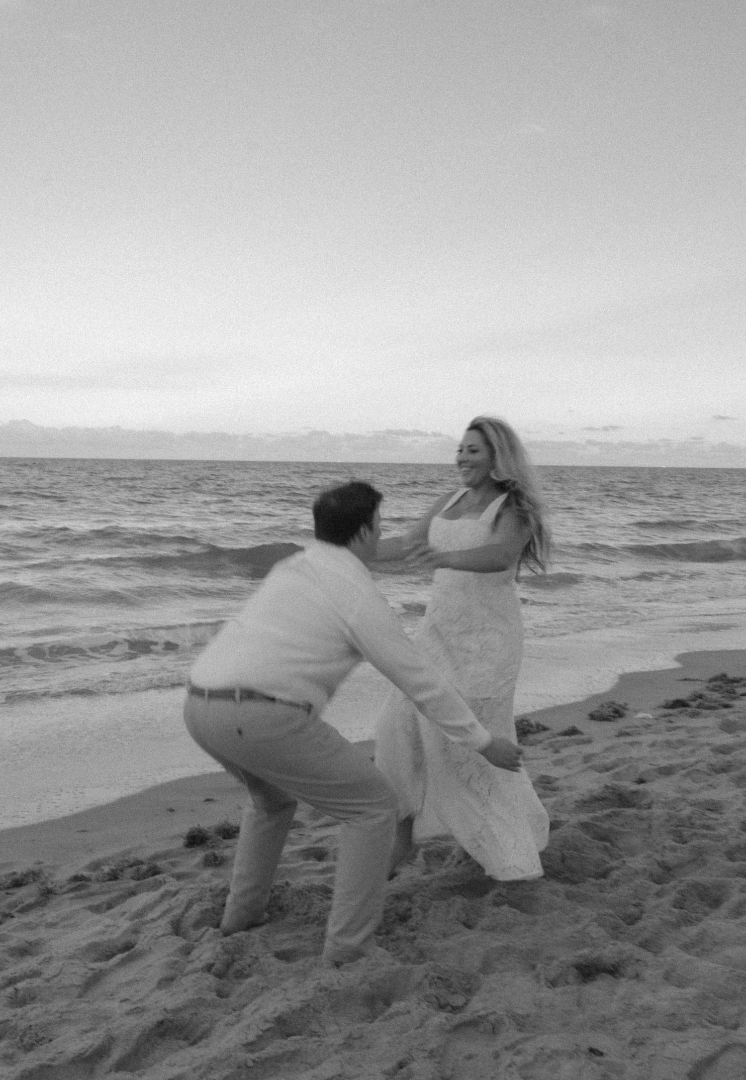 Black and white photo of a joyful couple playing on a sandy ocean beach.