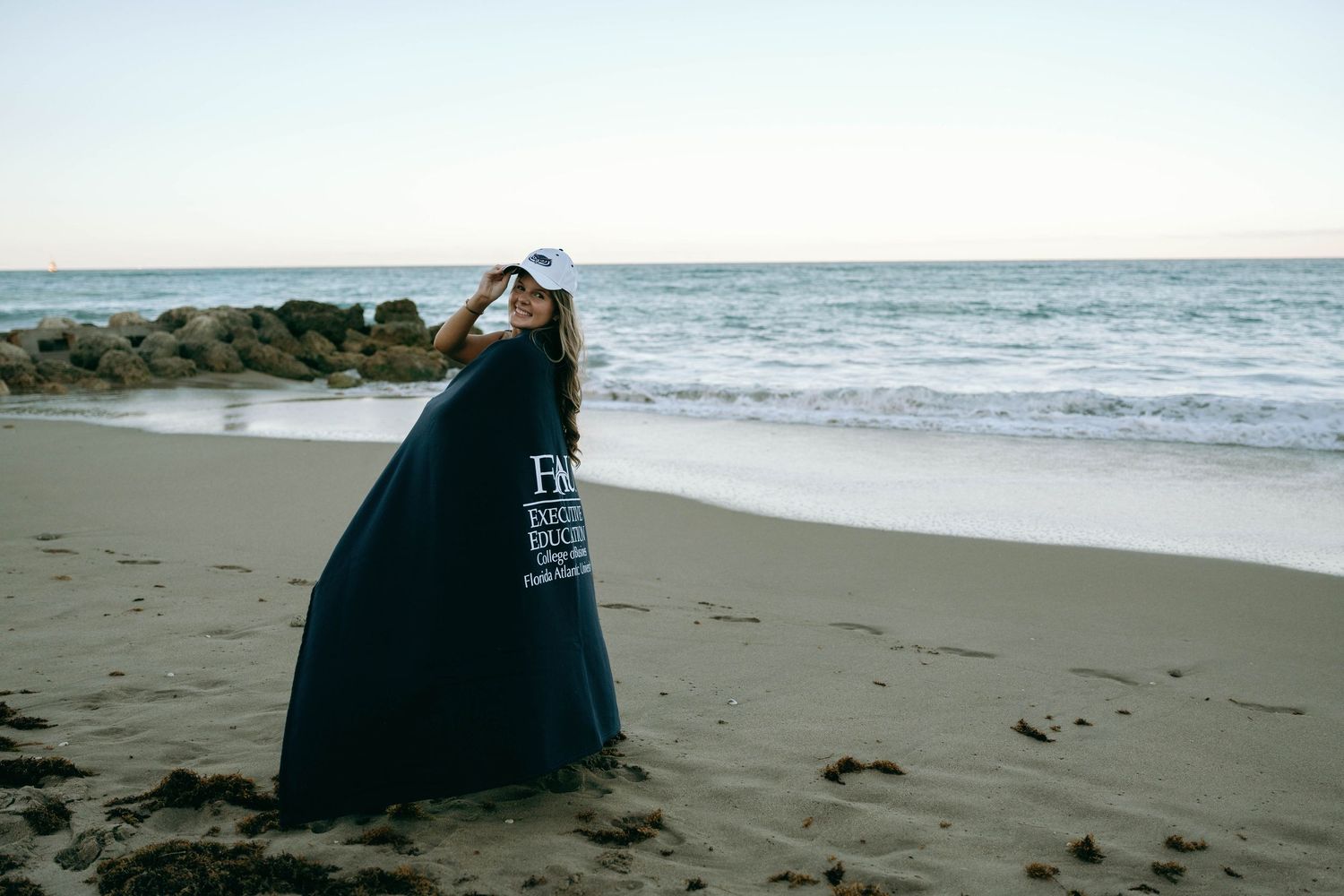Person wrapped in dark blanket standing on sandy beach at dusk with ocean waves. Worth Avenue, Palm Beach, FL