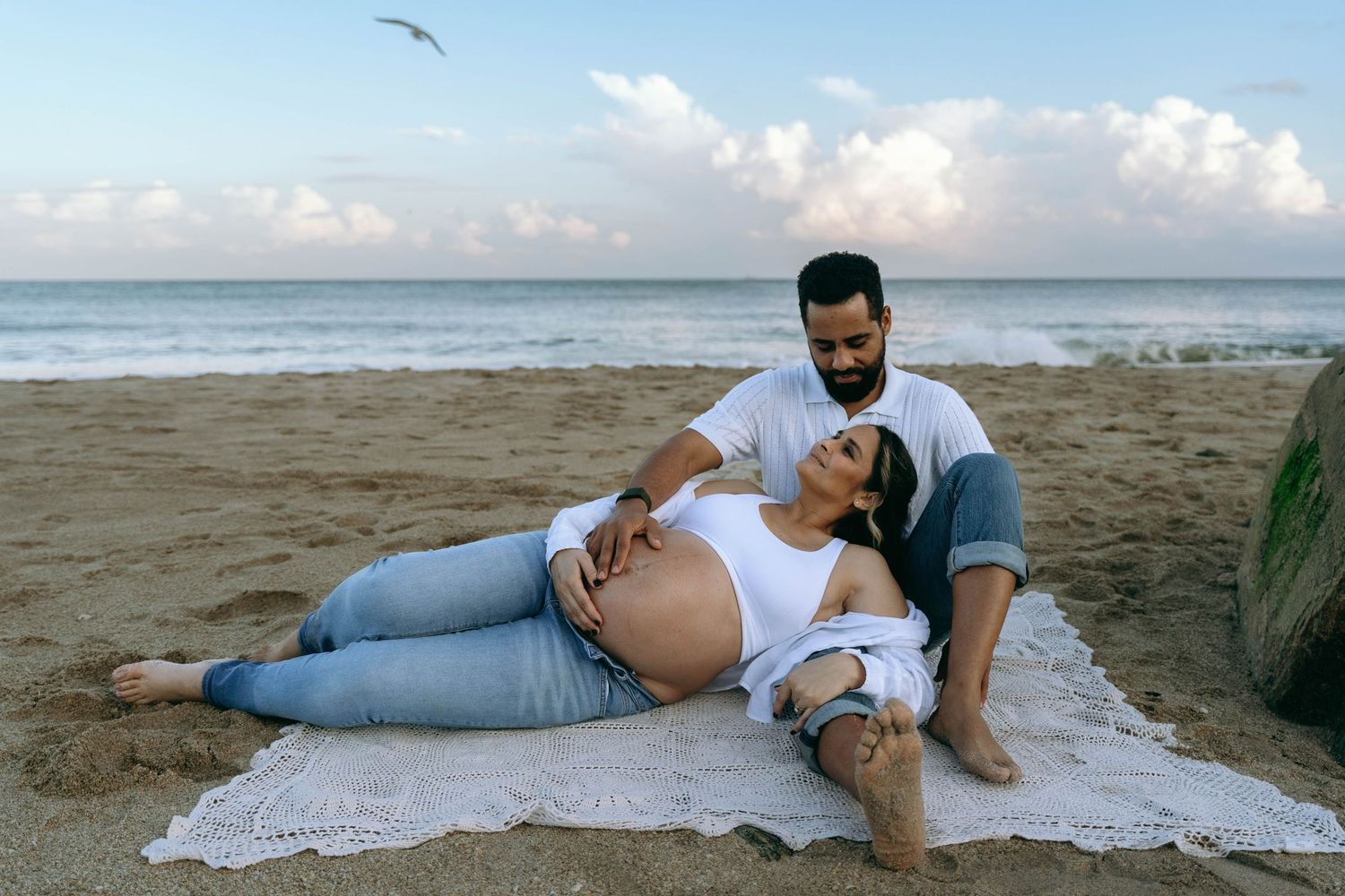 A couple relaxes on a beach blanket during their maternity photoshoot.