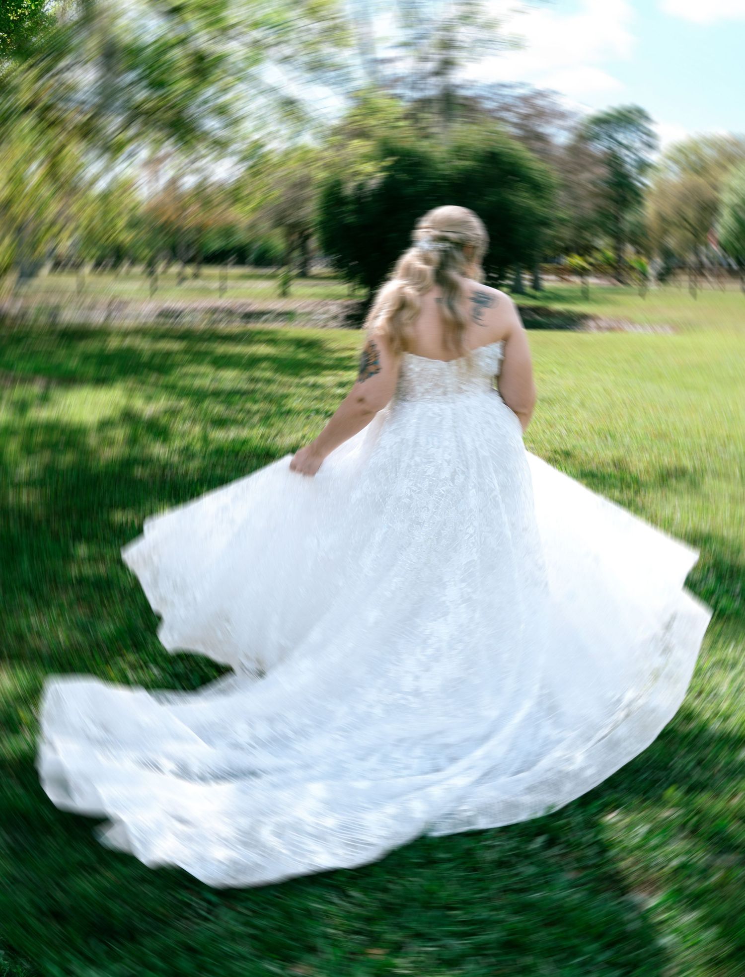 Bride twirling in flowing white lace wedding gown on green grass outdoor garden setting.
