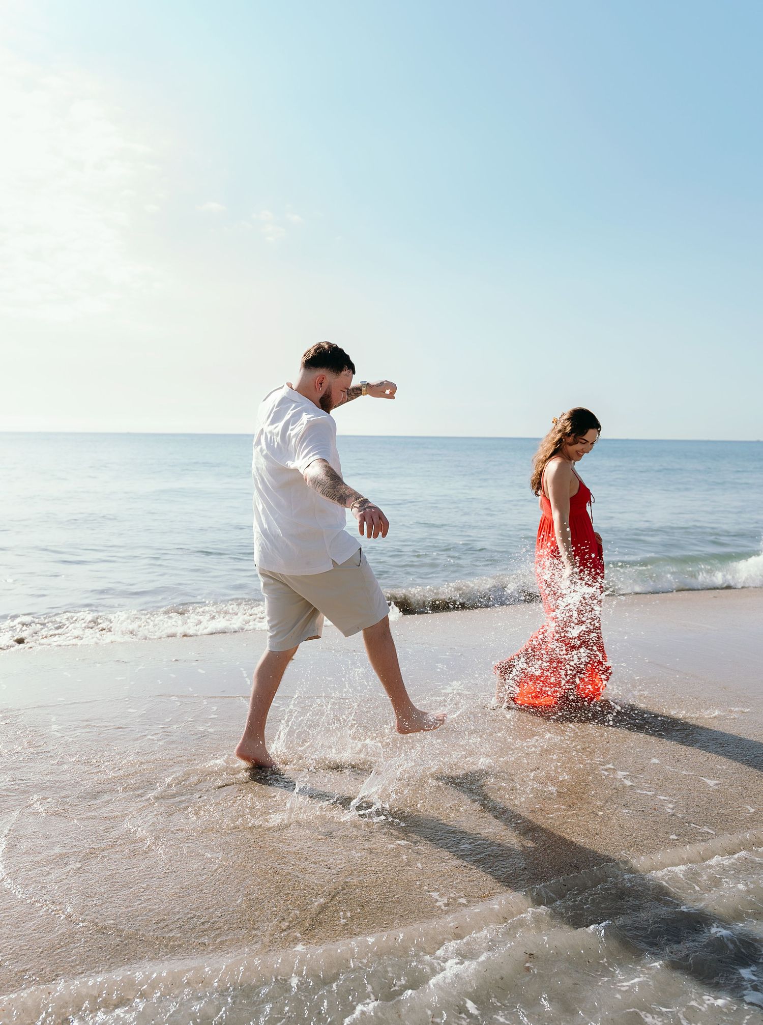 Couple splashing and playing in ocean waves at the beach.