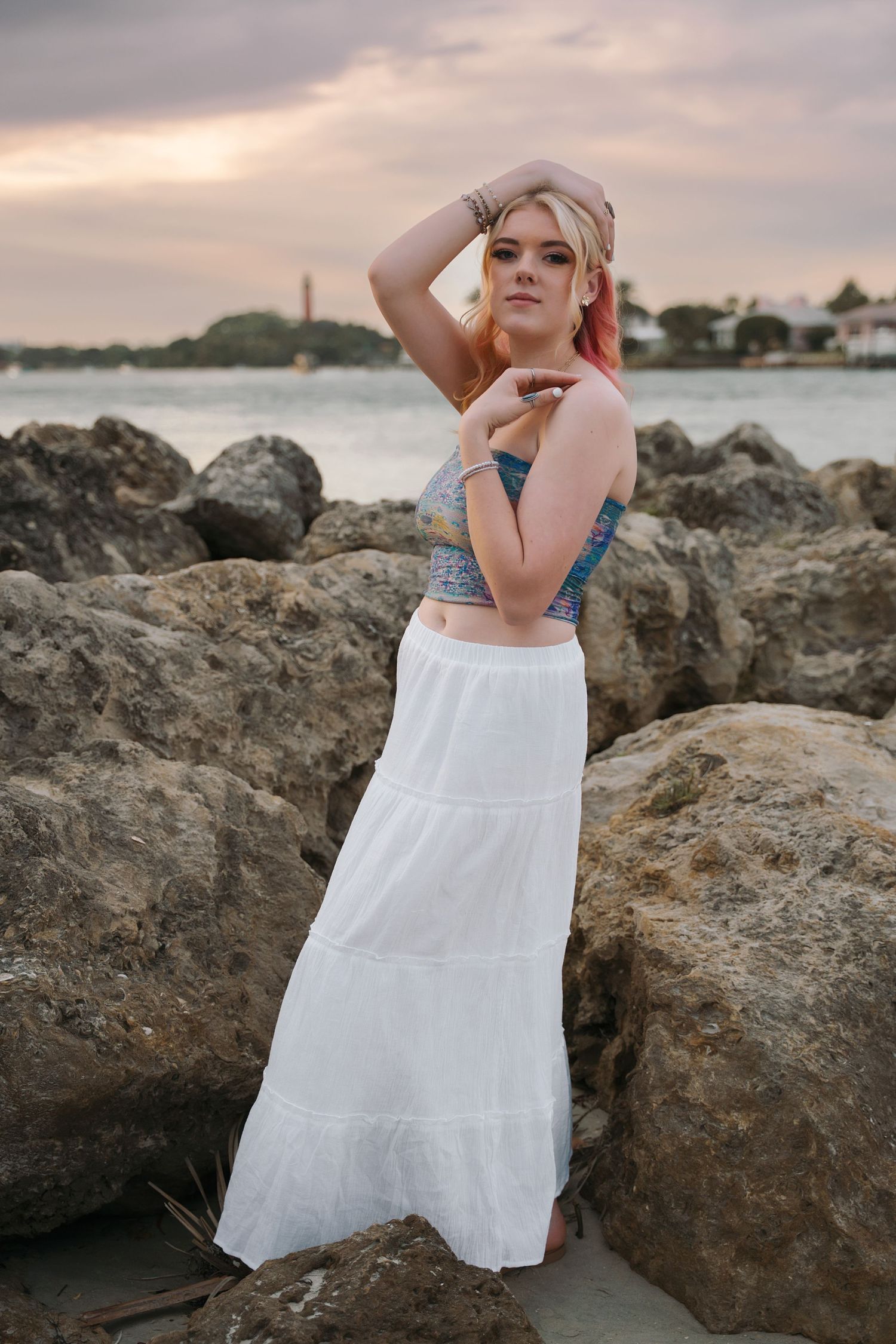 A coastal photoshoot featuring a white maxi skirt and blue top against rocky shoreline.