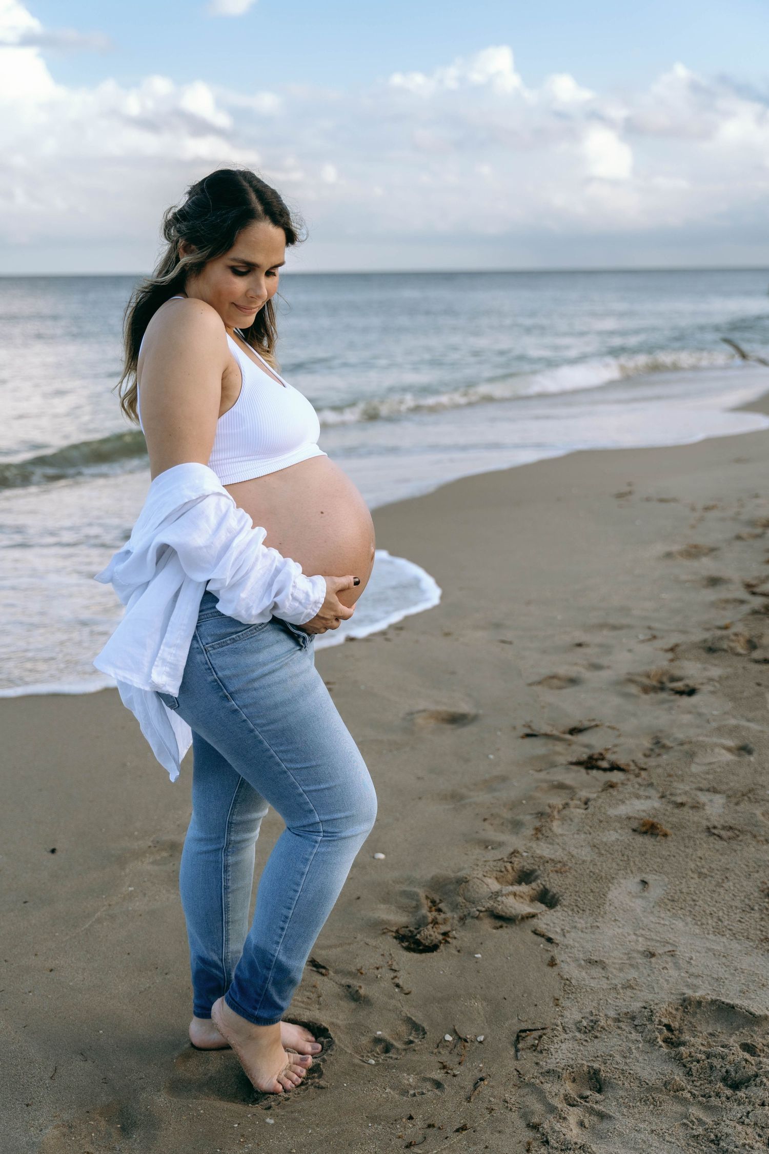 A woman in white and denim poses gracefully on a peaceful beach setting.