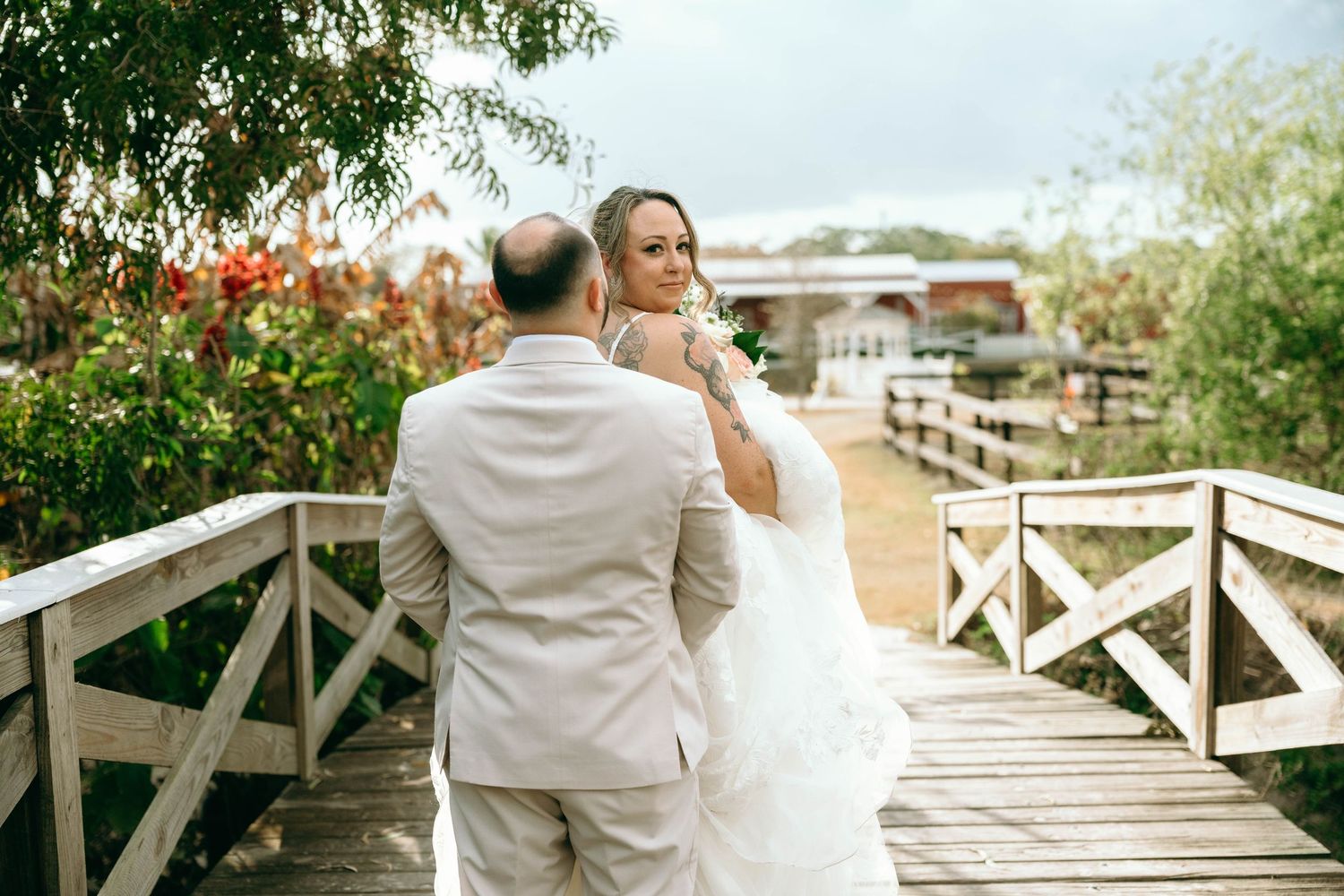 Couple in formal attire sharing romantic moments on a wooden boardwalk surrounded by lush greenery.
