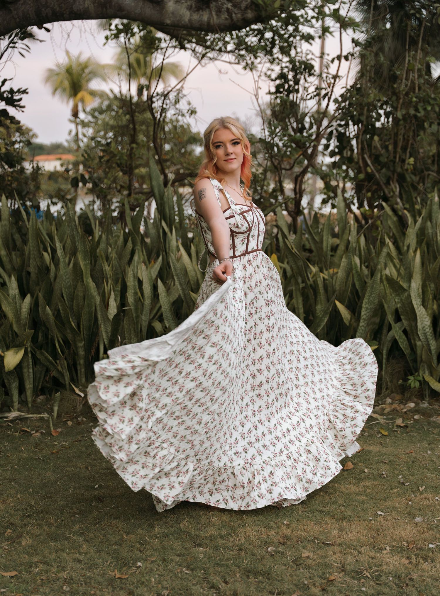 A flowing white patterned maxi dress twirls gracefully in a tropical garden setting with palm trees.