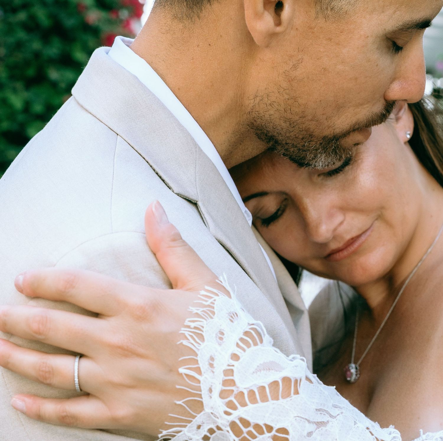 Bride and groom sharing tender embrace, bride in lace dress with diamond necklace.