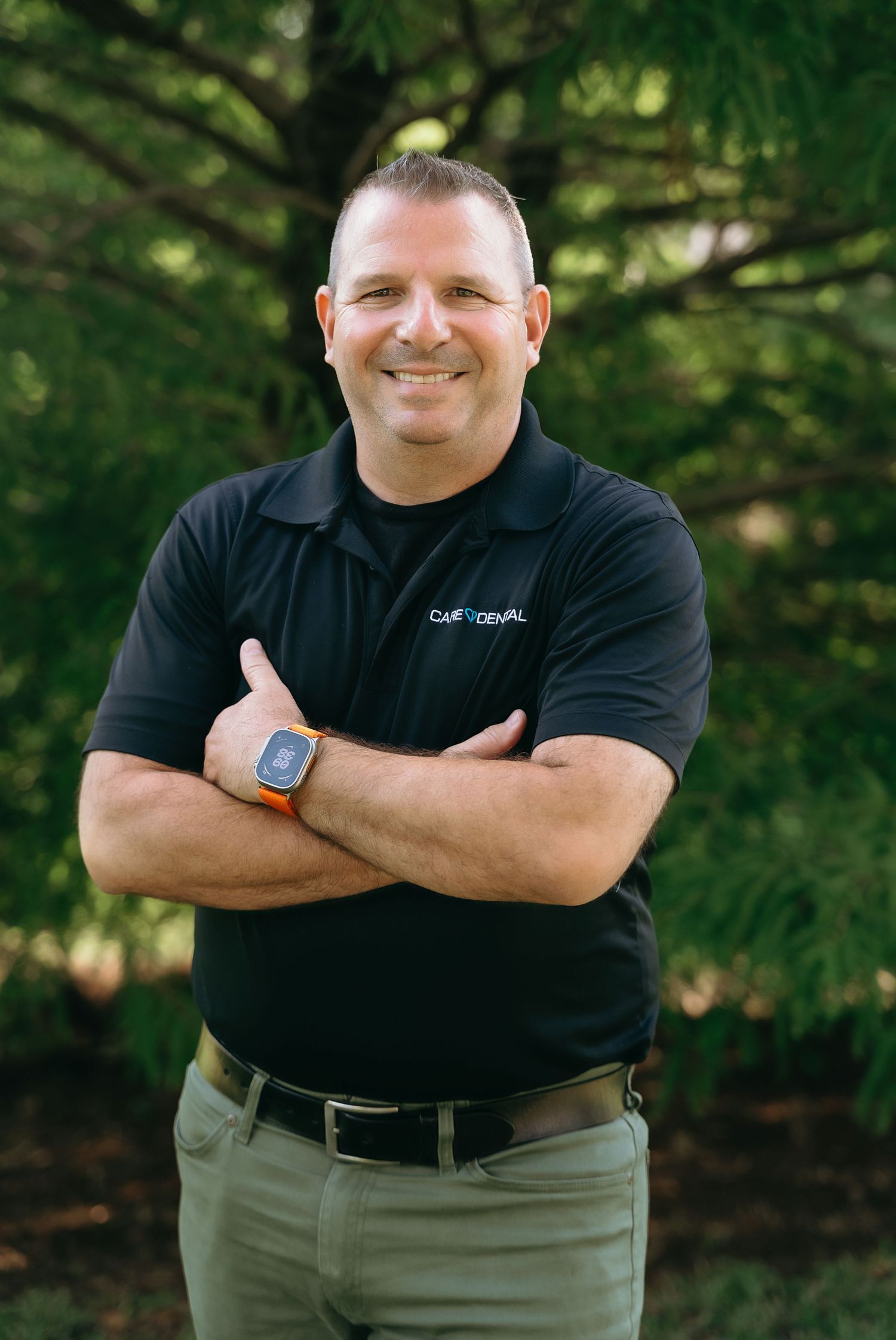 Professional headshots of someone in black polo shirt with company branding against natural backdrop.