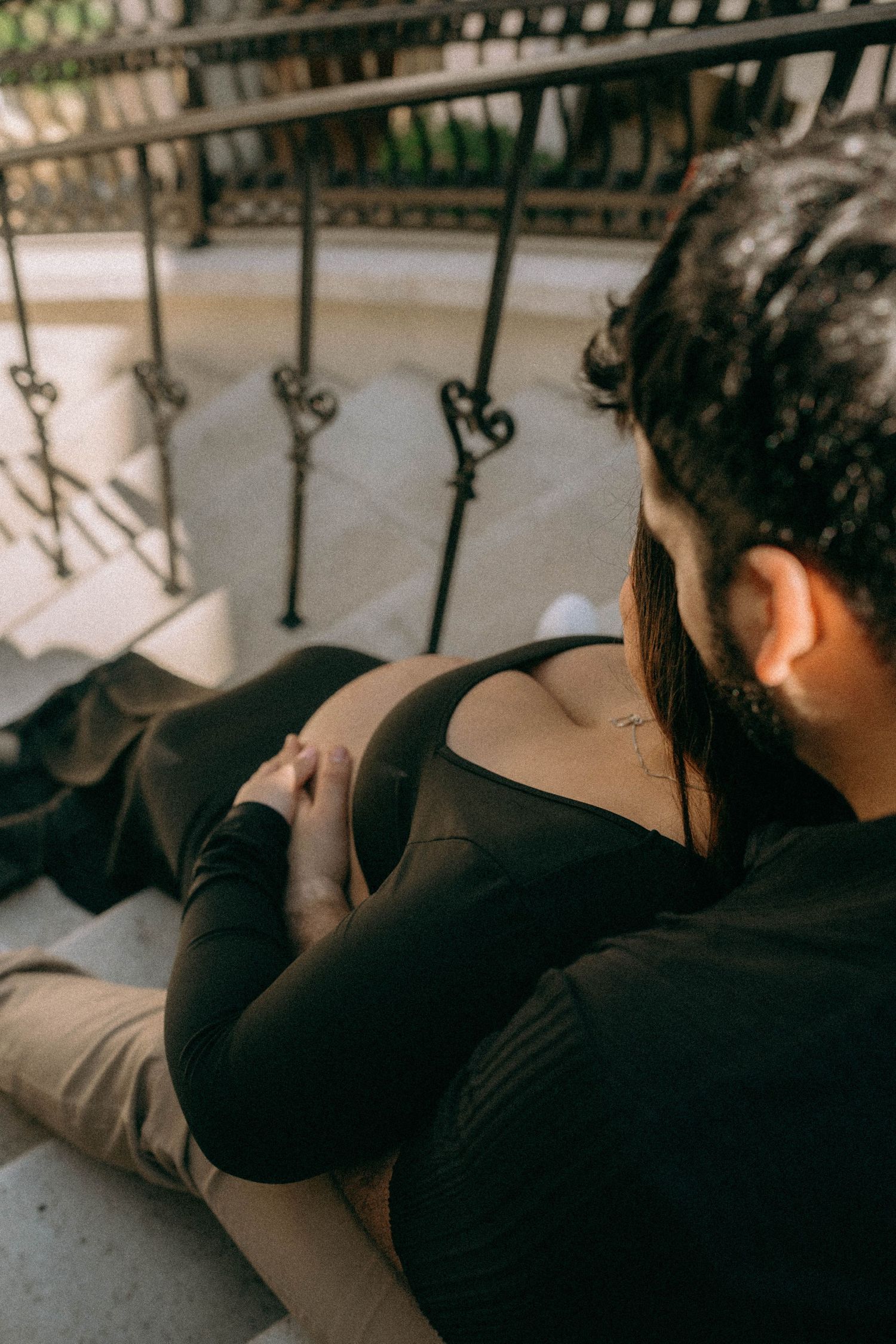 Couple sharing intimate moment on balcony steps, man tenderly holding pregnant woman's belly outdoors. Worth Avenue, Palm Beach, FL