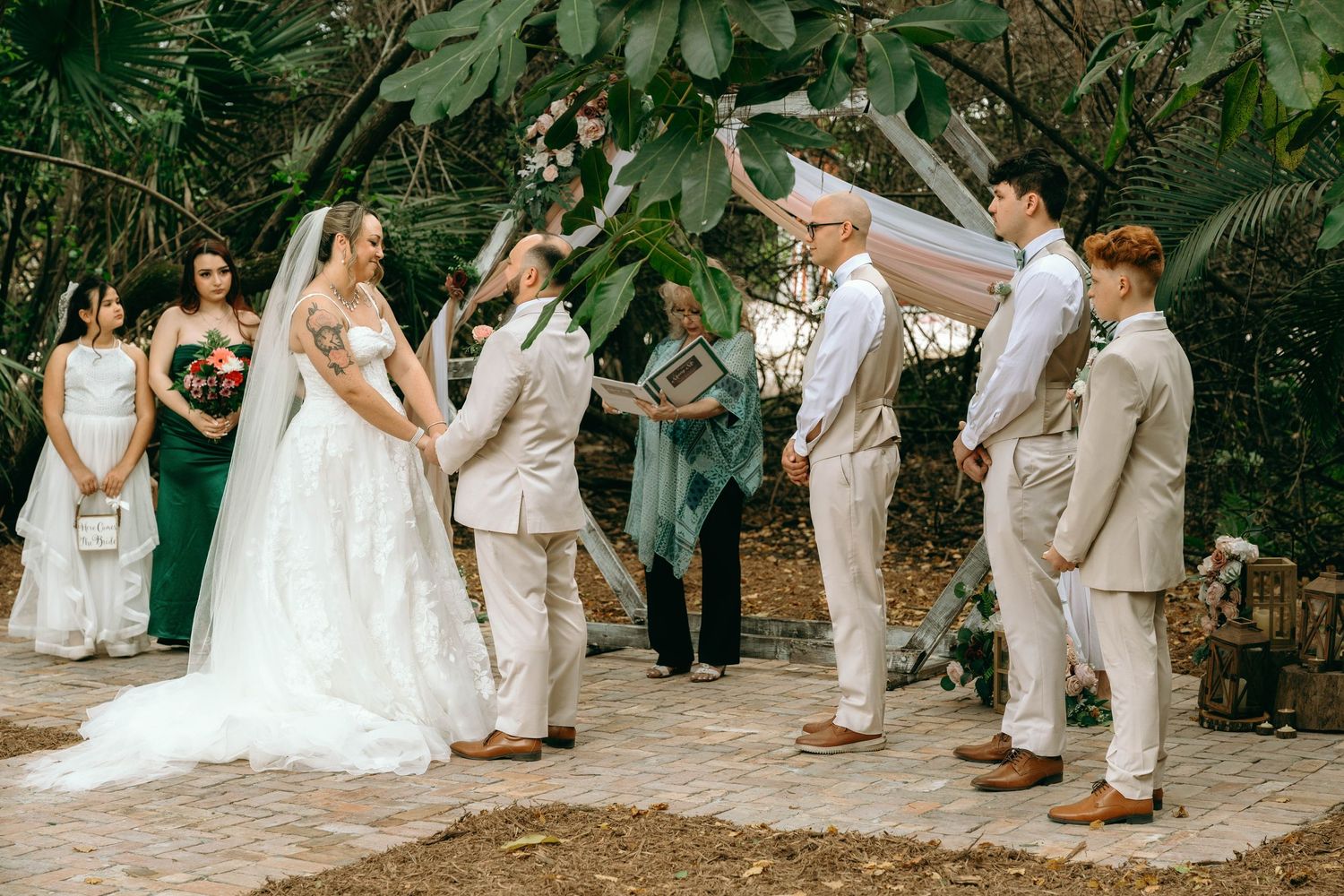 Wedding party members in light colored attire pose together on a rustic outdoor path.