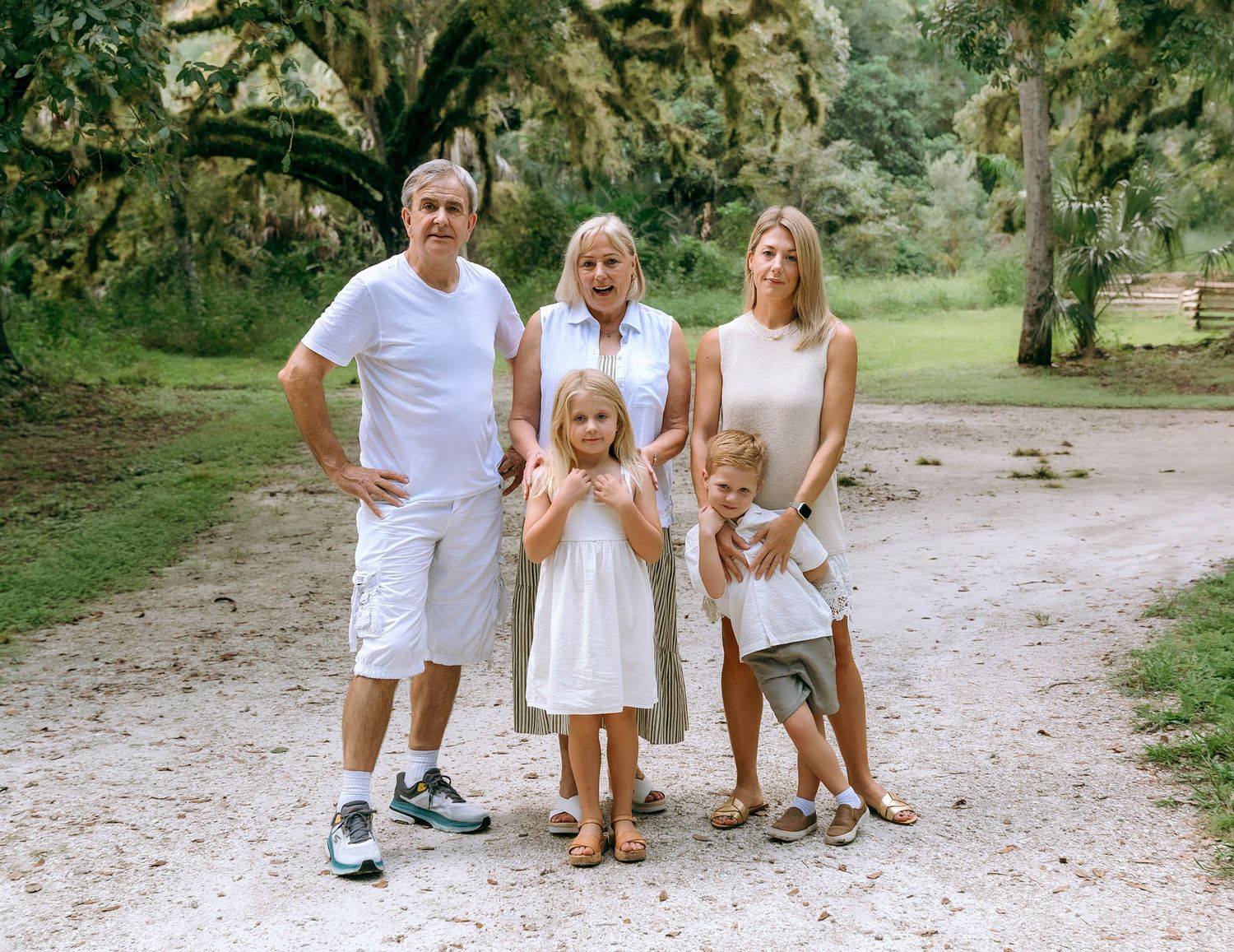 Family in white outfits playing together on a grassy path in a natural outdoor setting.