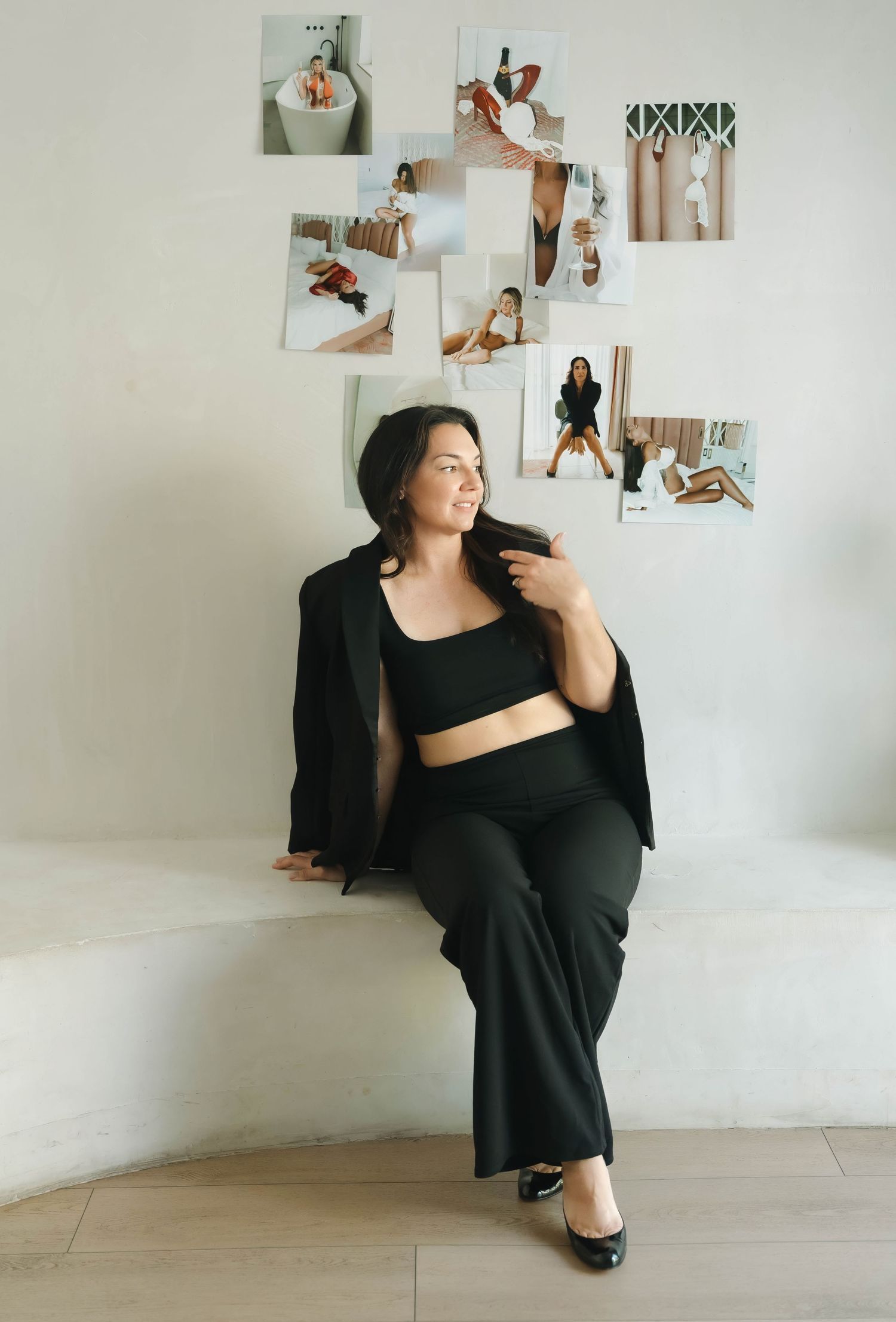 A woman in black poses confidently near a wall decorated with artistic photographs.