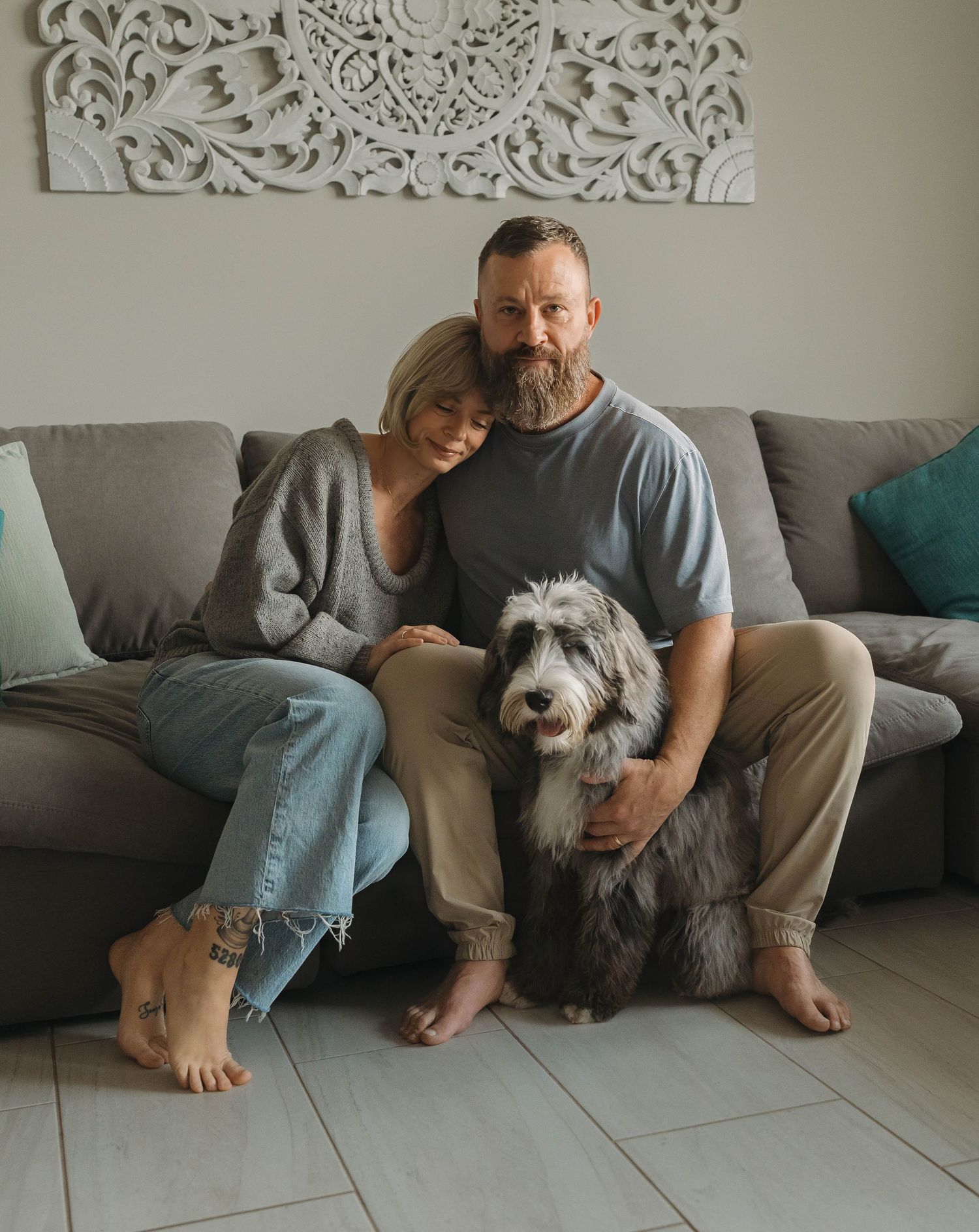 A cozy family scene on a grey couch with a fluffy dog and decorative wall art.