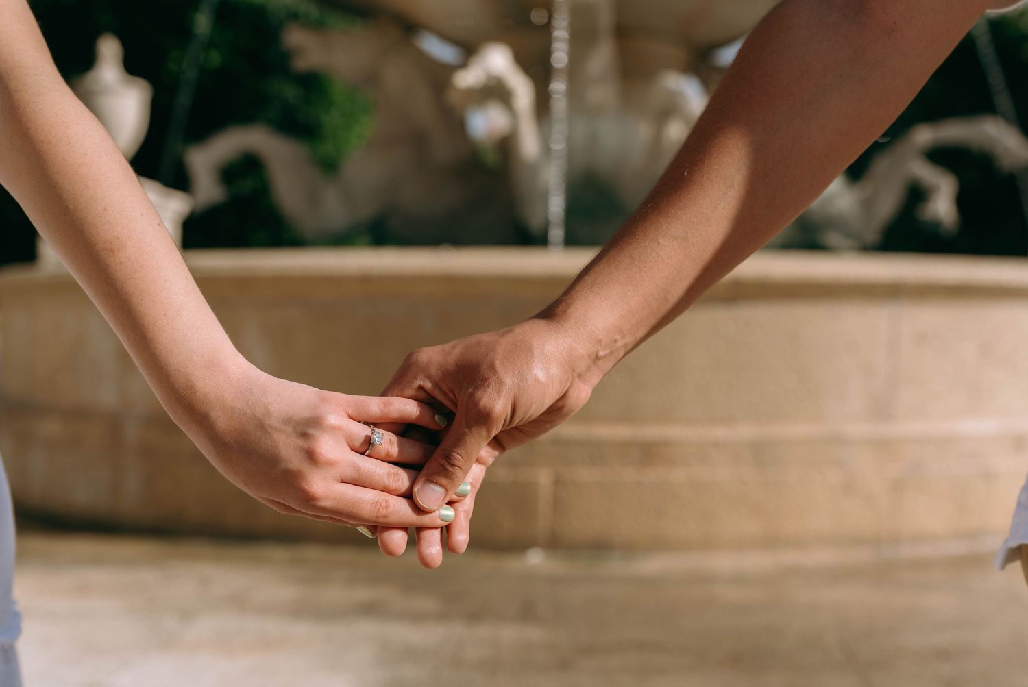 Couple holding hands tenderly near a decorative stone fountain, symbolizing love and connection. Engagement photos on Worth Avenue