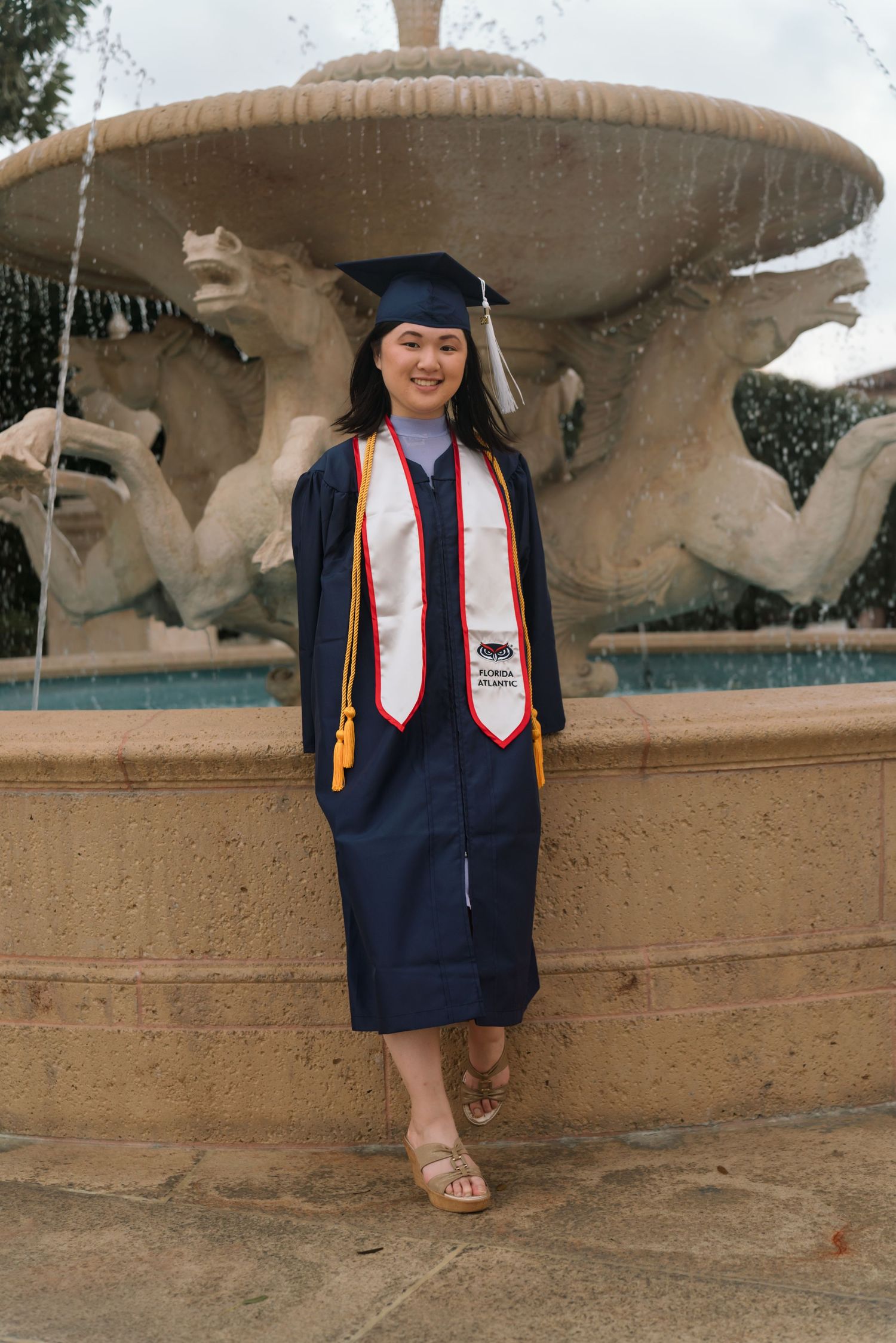A navy graduation cap and gown photographed by a decorative stone fountain.