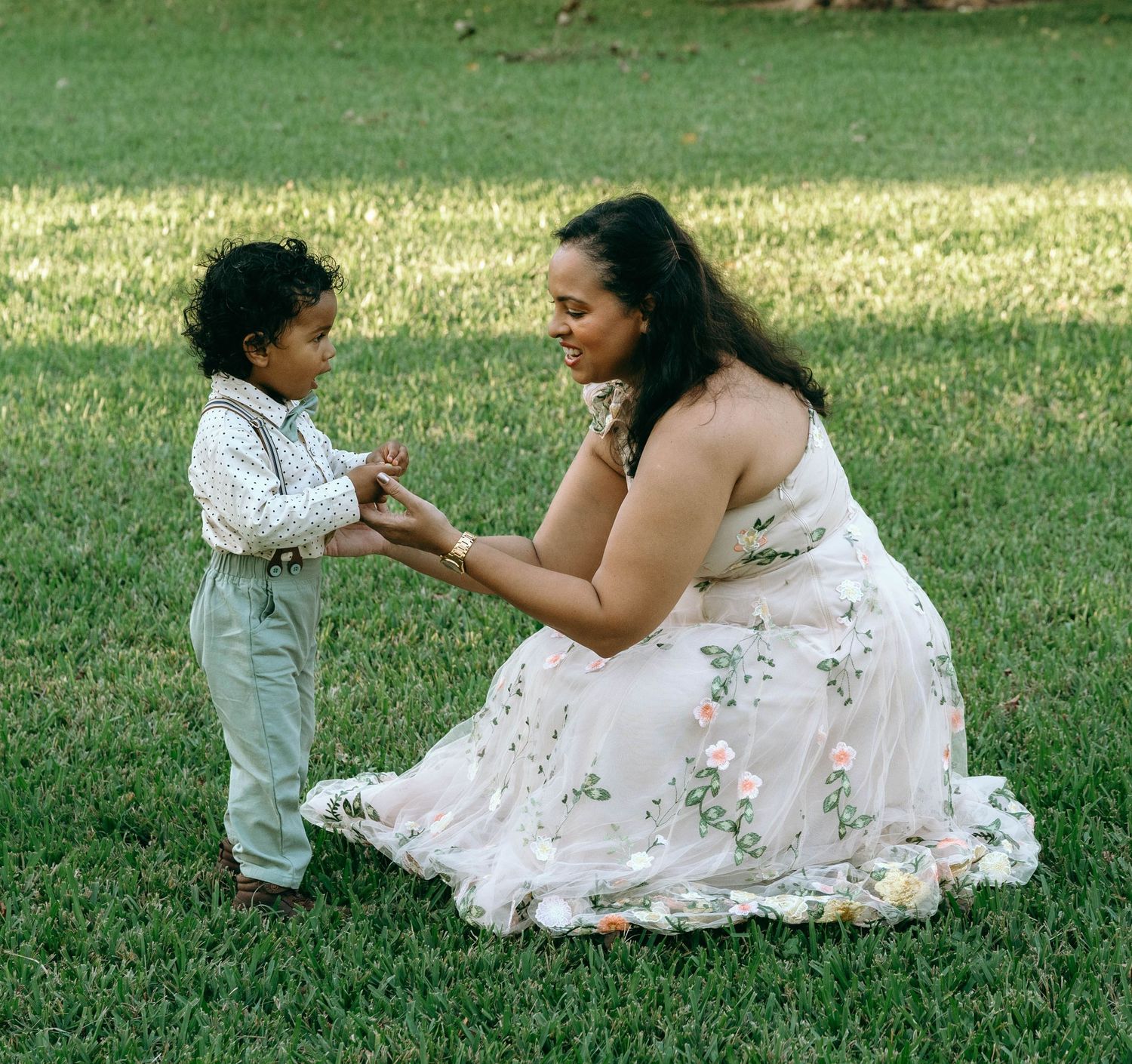 A tender moment shared between two people on a grassy lawn, one wearing a white floral dress and the other in light clothing.