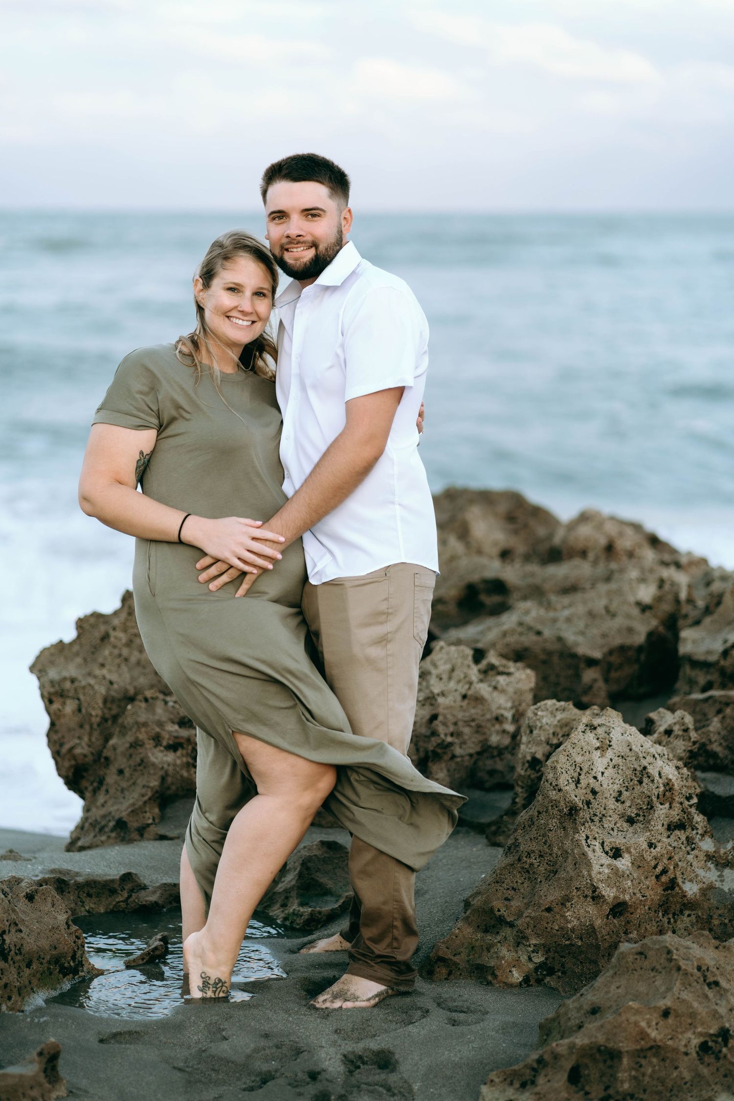 Couple poses intimately on volcanic rocks by the ocean during a beach photoshoot.